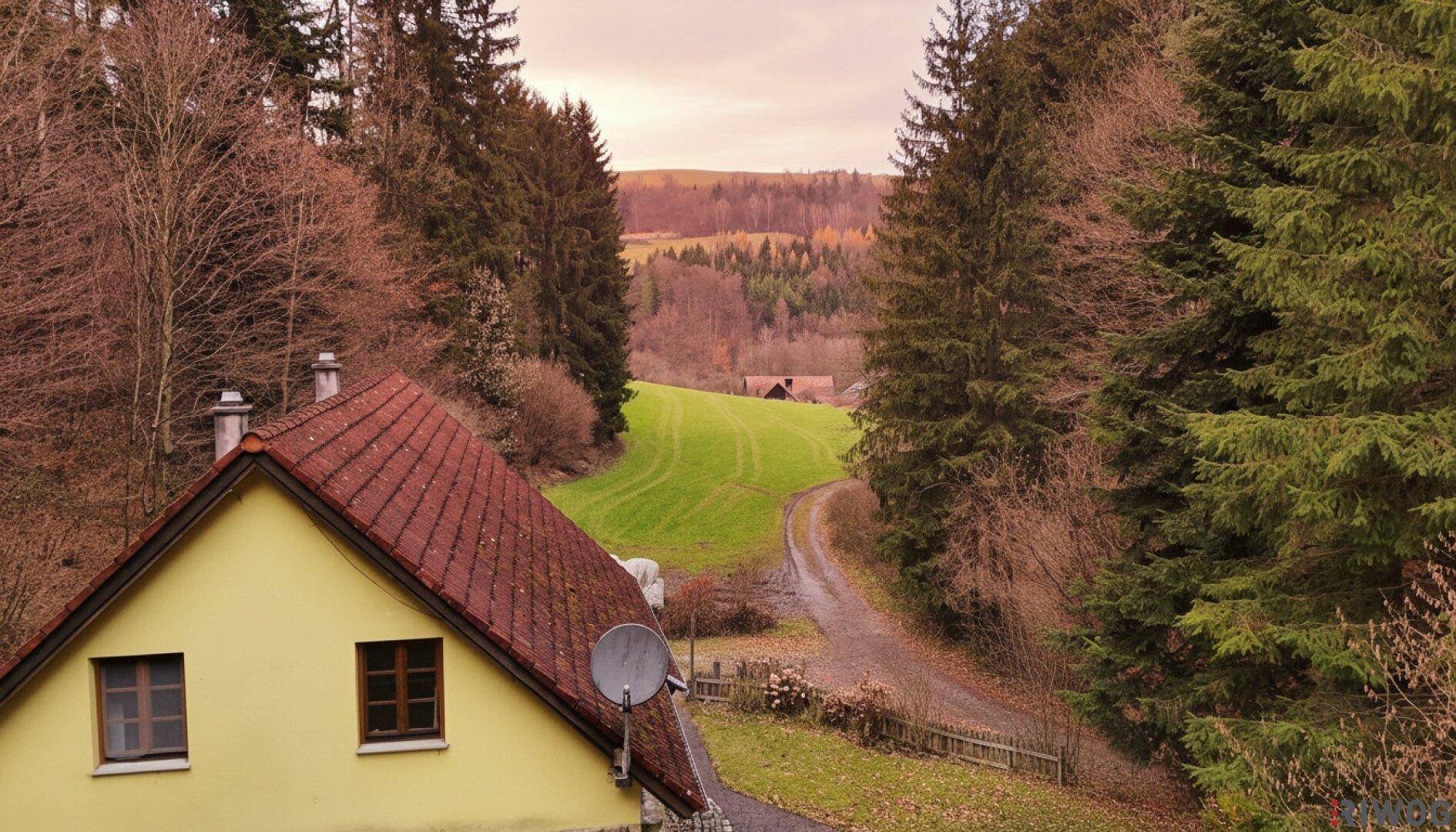 Haus mit rotem Ziegeldach in ländlicher Umgebung, umgeben von Wäldern und grünen Hügeln.