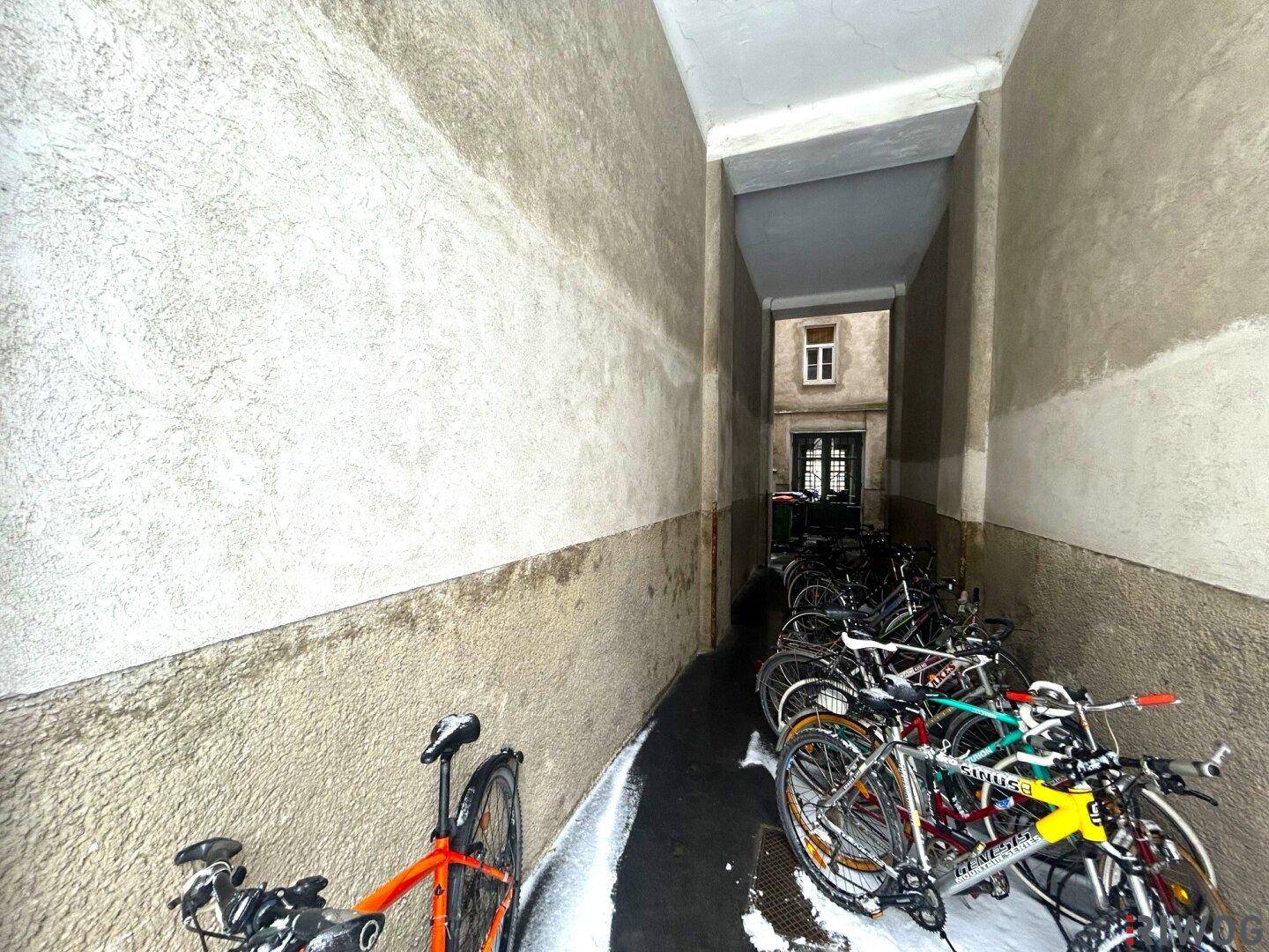 Schmaler Durchgang im Freien, der als Fahrradabstellraum genutzt wird, mit Schnee auf dem Boden.