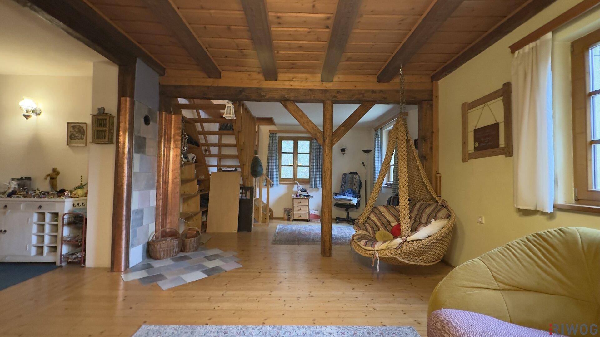 Offener Wohnbereich mit sichtbaren Holzbalken, Holzfußboden und einer gemütlichen Hängeschaukel.