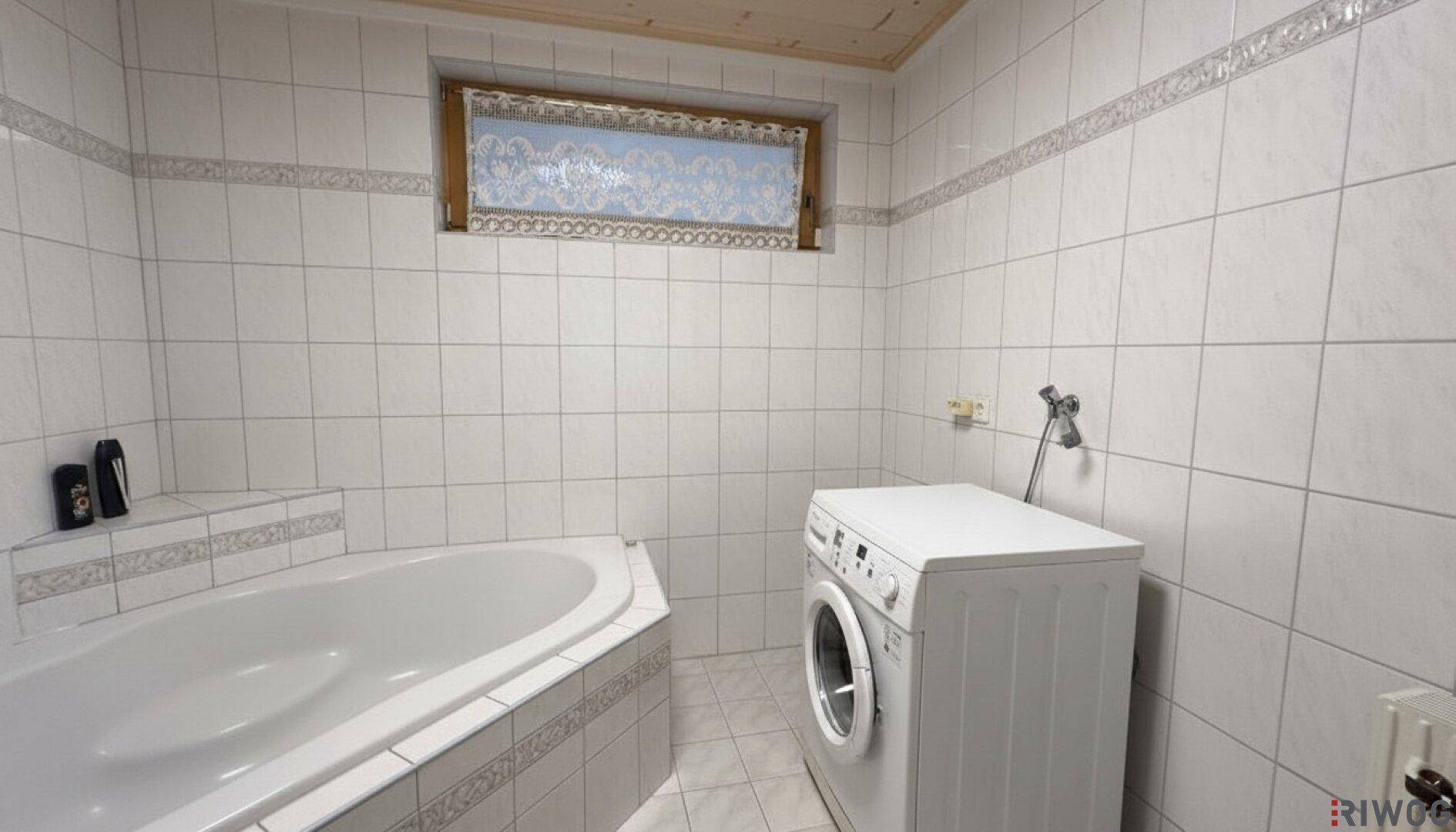 Gefliestes Badezimmer mit Eckbadewanne, Waschmaschine und Fenster.