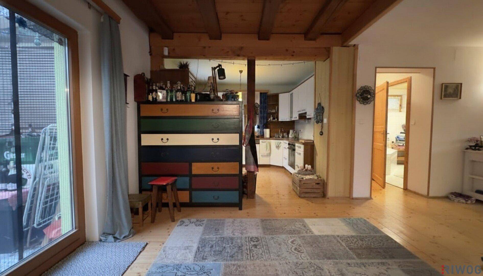 Geräumiger Wohnbereich mit Holzbalkendecke, Holzboden und Zugang zum Außenbereich.