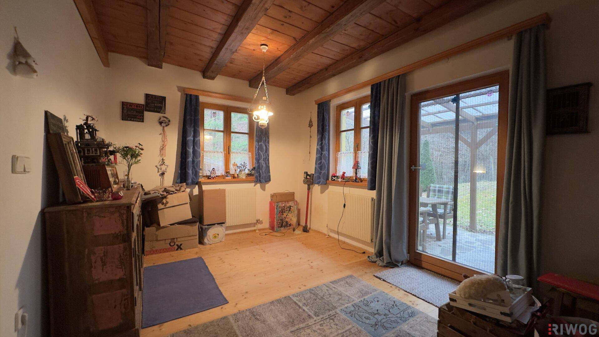 Heller Raum mit Holzboden, Holzbalkendecke und direktem Zugang zum Gartenbereich.