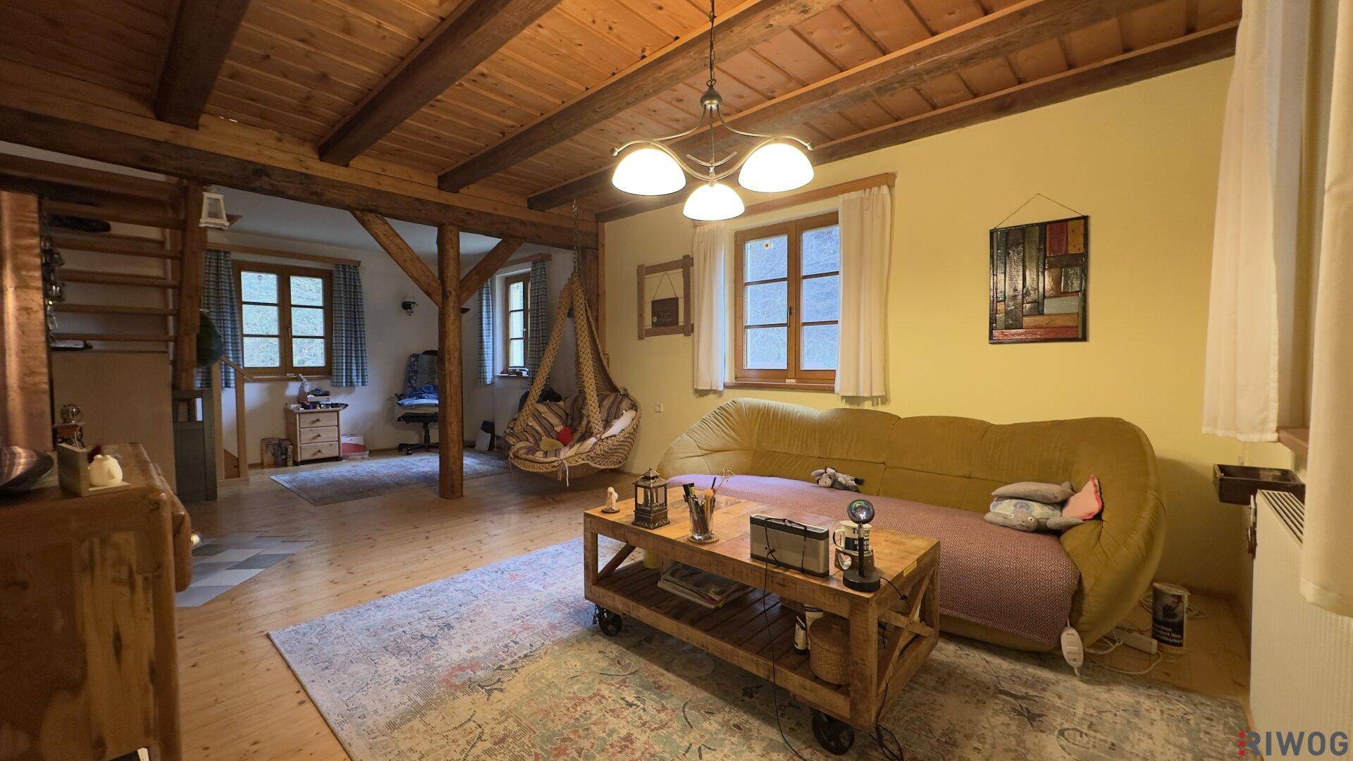 Gemütliches Wohnzimmer mit Holzbalkendecke, Holzboden und bequemer Couch.