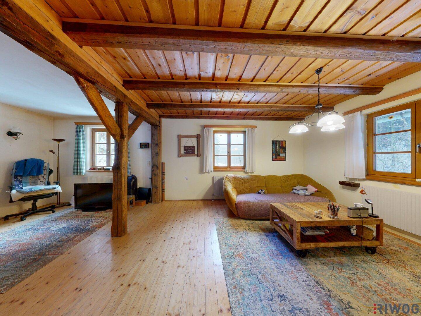 Gemütliches Wohnzimmer mit sichtbaren Holzbalken, Holzboden und großem Teppich.