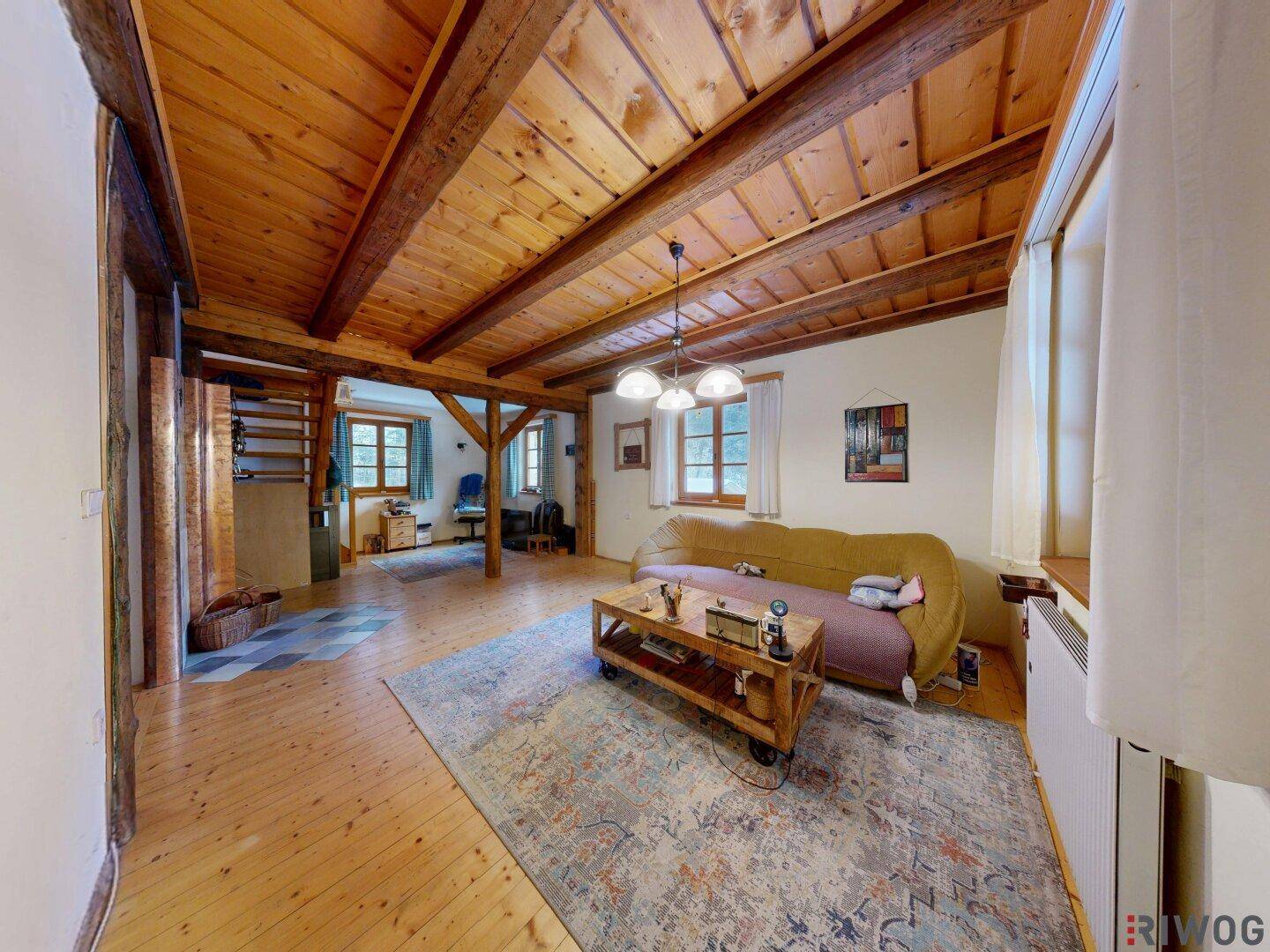 Helles Wohnzimmer mit rustikalen Holzbalken, Holzboden und traditionellem Teppich.