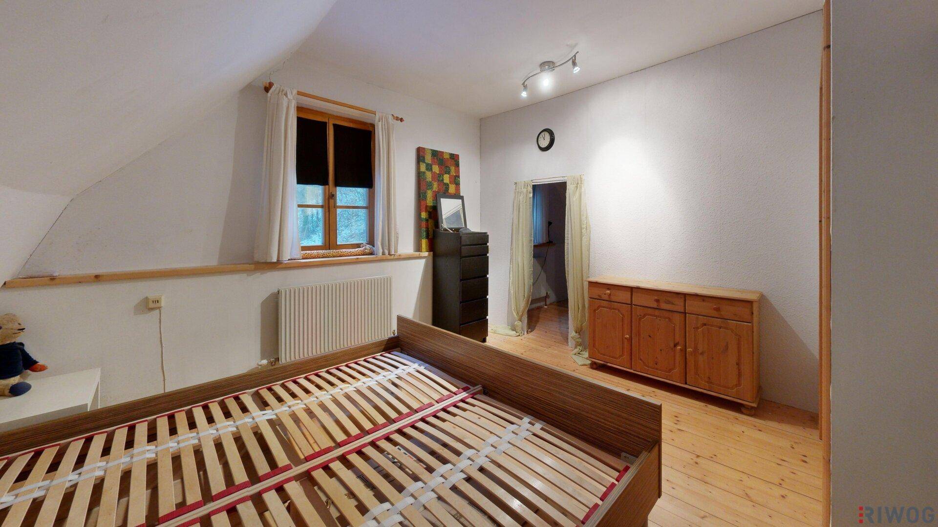 Schlafzimmer mit Holzboden, schrägen Wänden und Blick ins Grüne durch das Fenster.