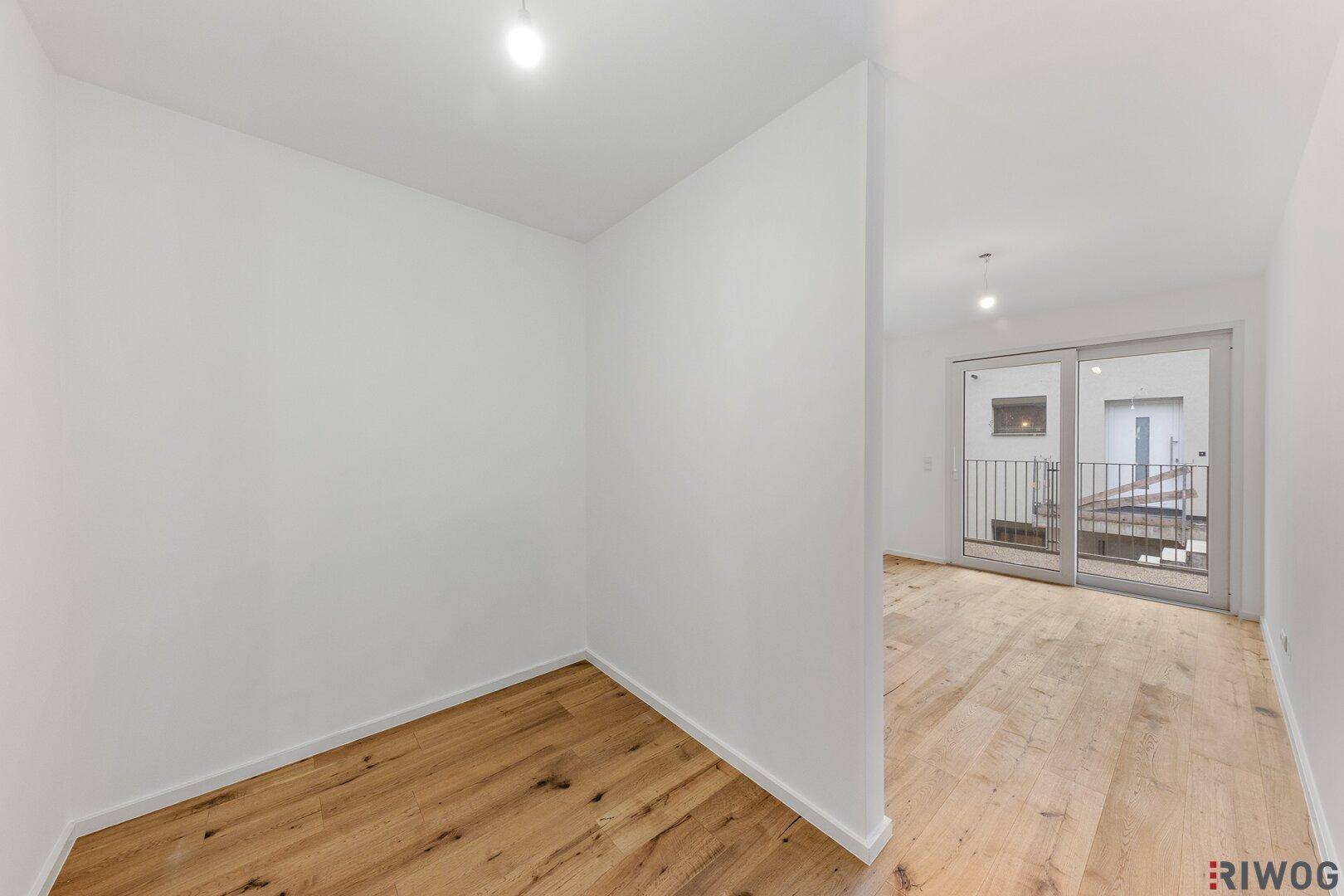 Geräumiger, heller Raum mit Holzboden und Schiebetür zum Balkon, ideal für Wohnzwecke.