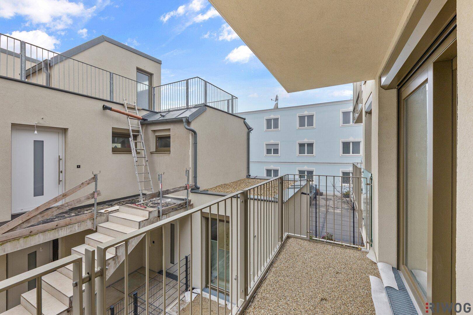 Balkon mit Kiesbelag und Metallgeländer, umgeben von weiteren Gebäudeteilen im Bau.