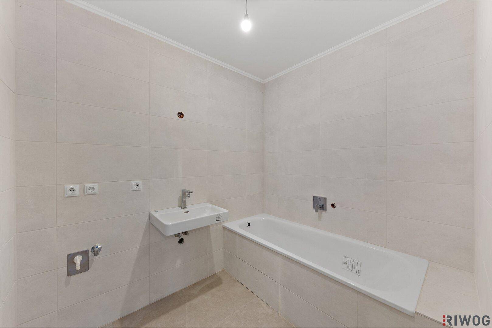 Modernes Badezimmer mit Badewanne und Waschbecken, hell gefliest und unbenutzt.