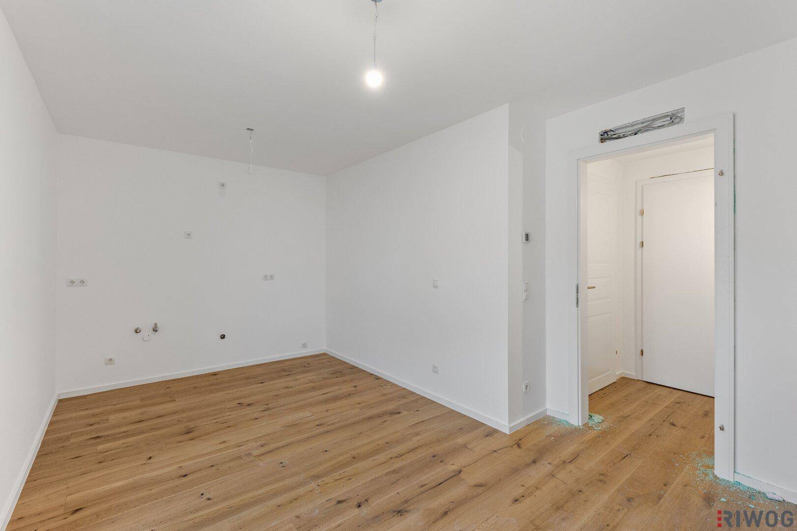 Helles Zimmer mit Holzfußboden und weißen Wänden, bereit für den Innenausbau.