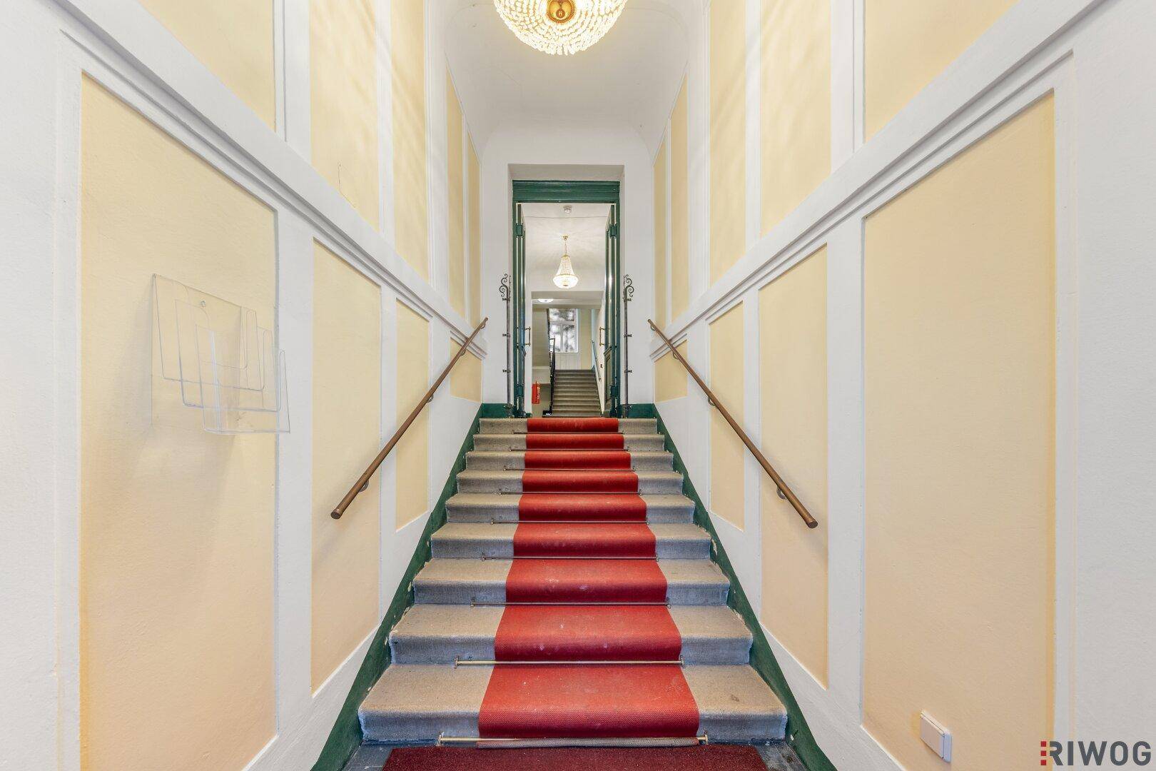 Repräsentatives Treppenhaus mit rotem Teppich und klassischem Kronleuchter.