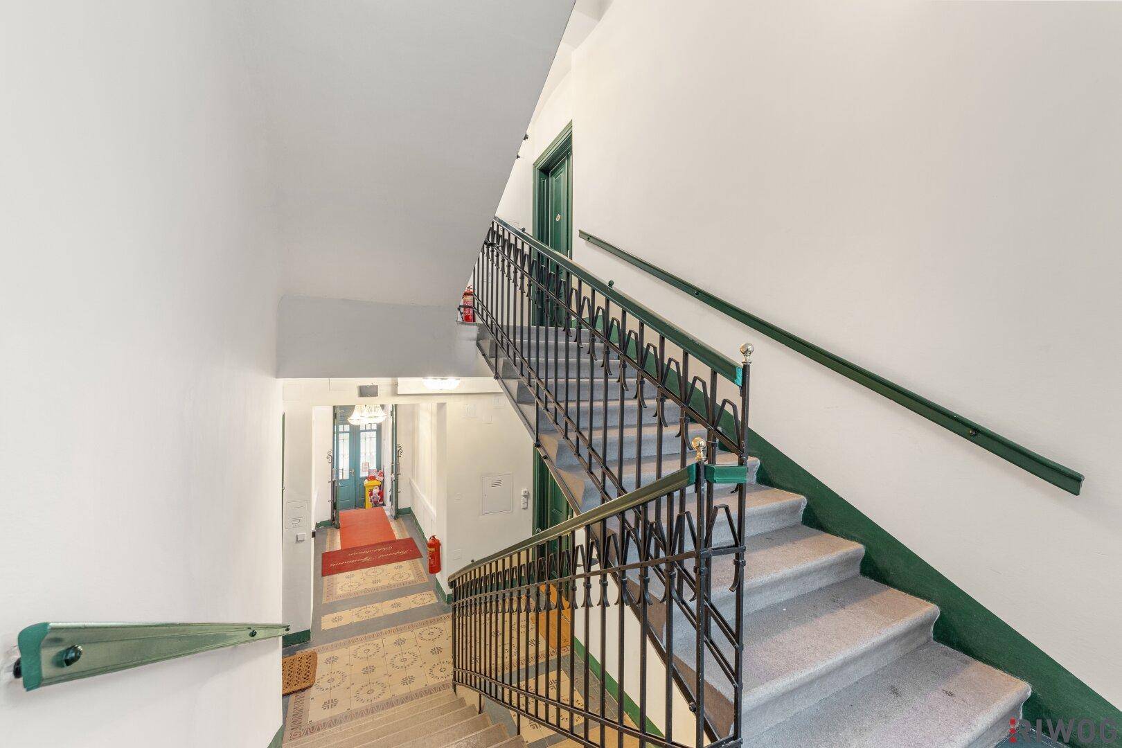 Historisches Treppenhaus mit schmiedeeisernem Geländer und Teppichboden in einem Altbau.