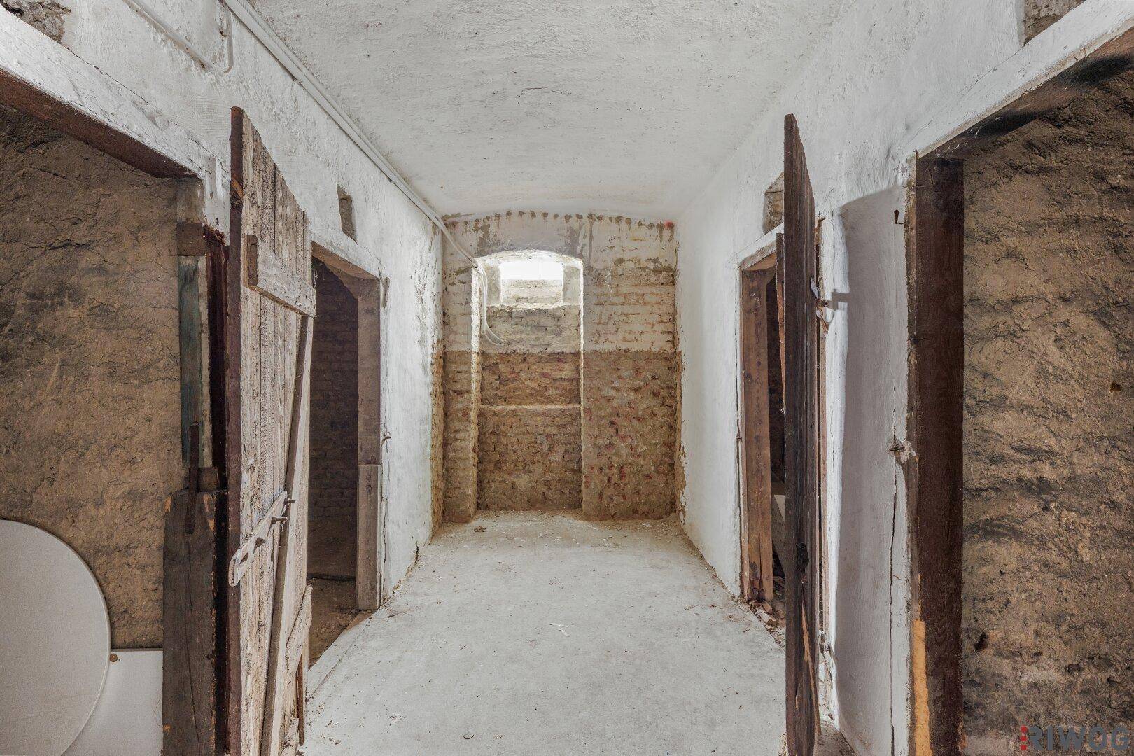Rustikaler Kellergang mit unverputzten Wänden und Holztüren, bietet Stauraum.