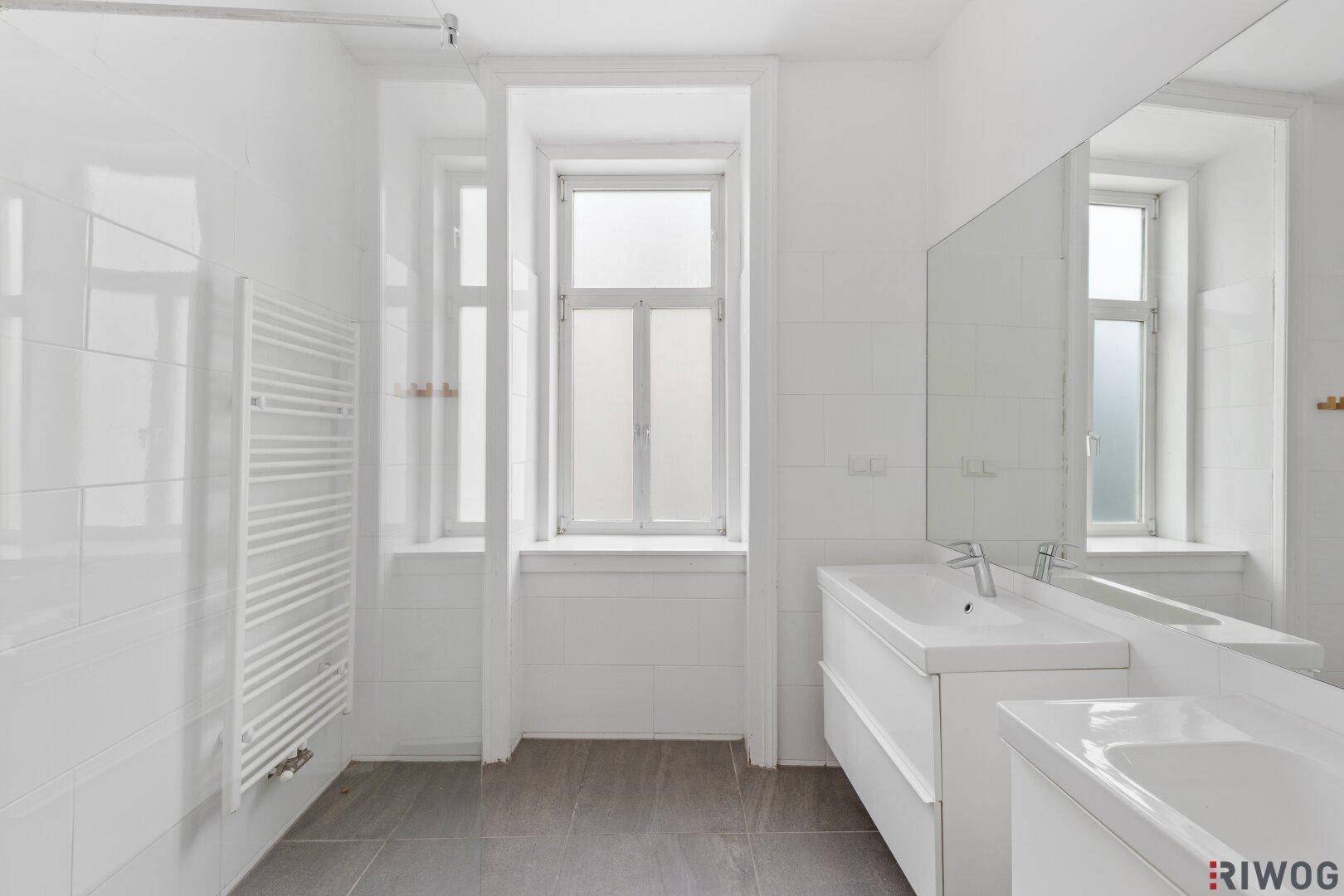 Modernes Badezimmer mit weißen Fliesen, Waschtisch und beheiztem Handtuchhalter.