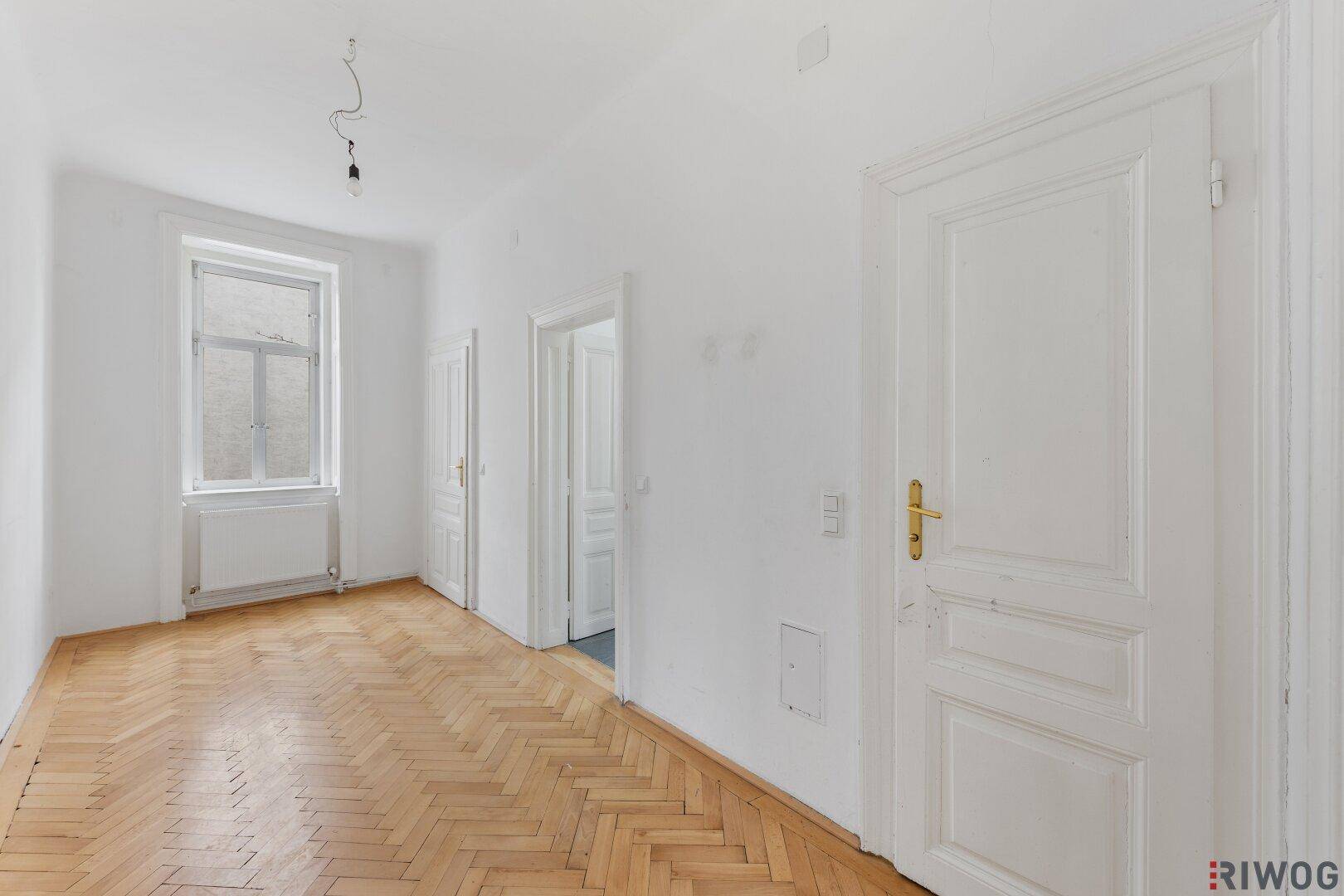 Heller Raum mit Fischgrätparkett und einer Tür zu einem weiteren Zimmer.