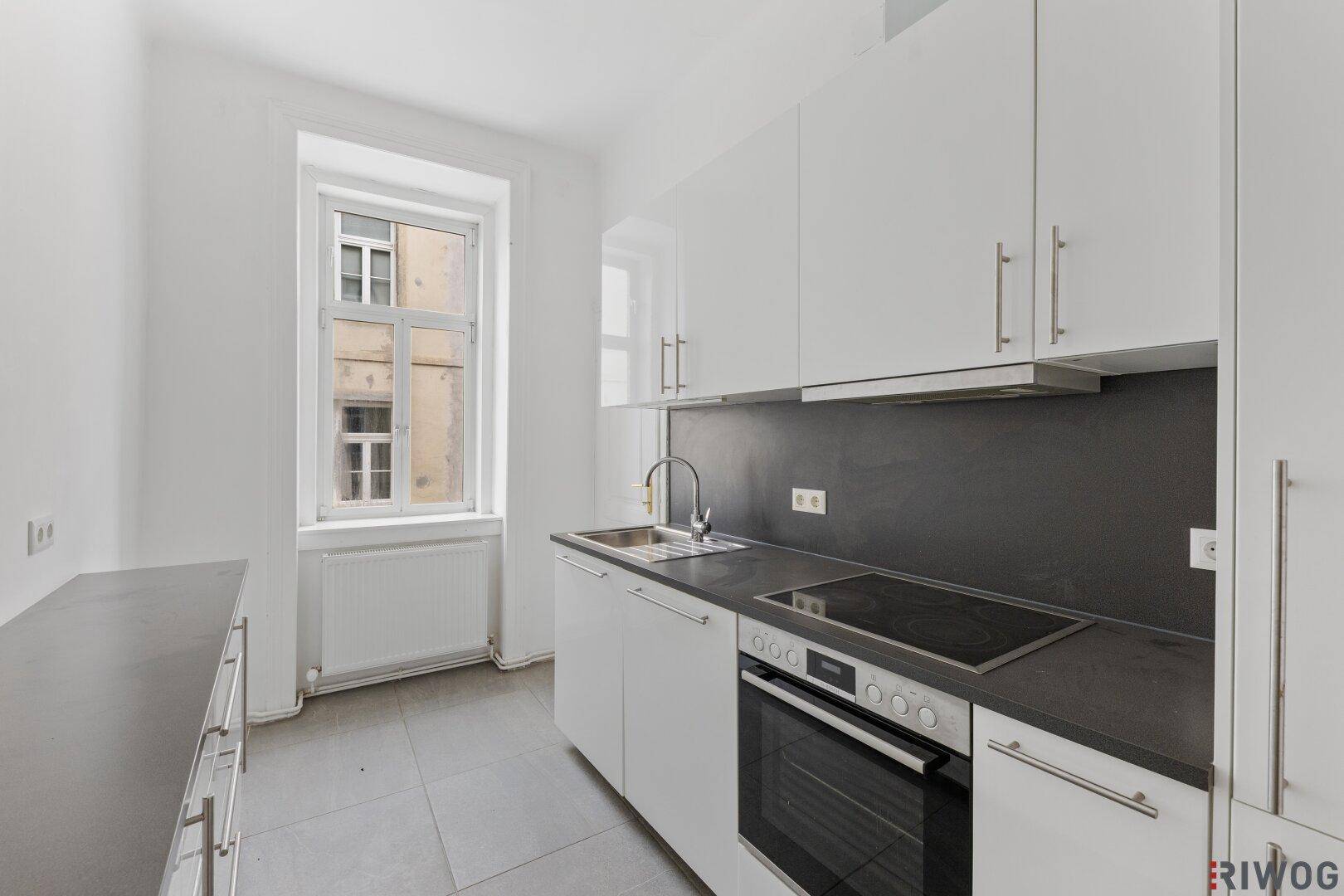Moderne Einbauküche mit weißen Hochglanzschränken, dunkler Arbeitsplatte und Fenster.