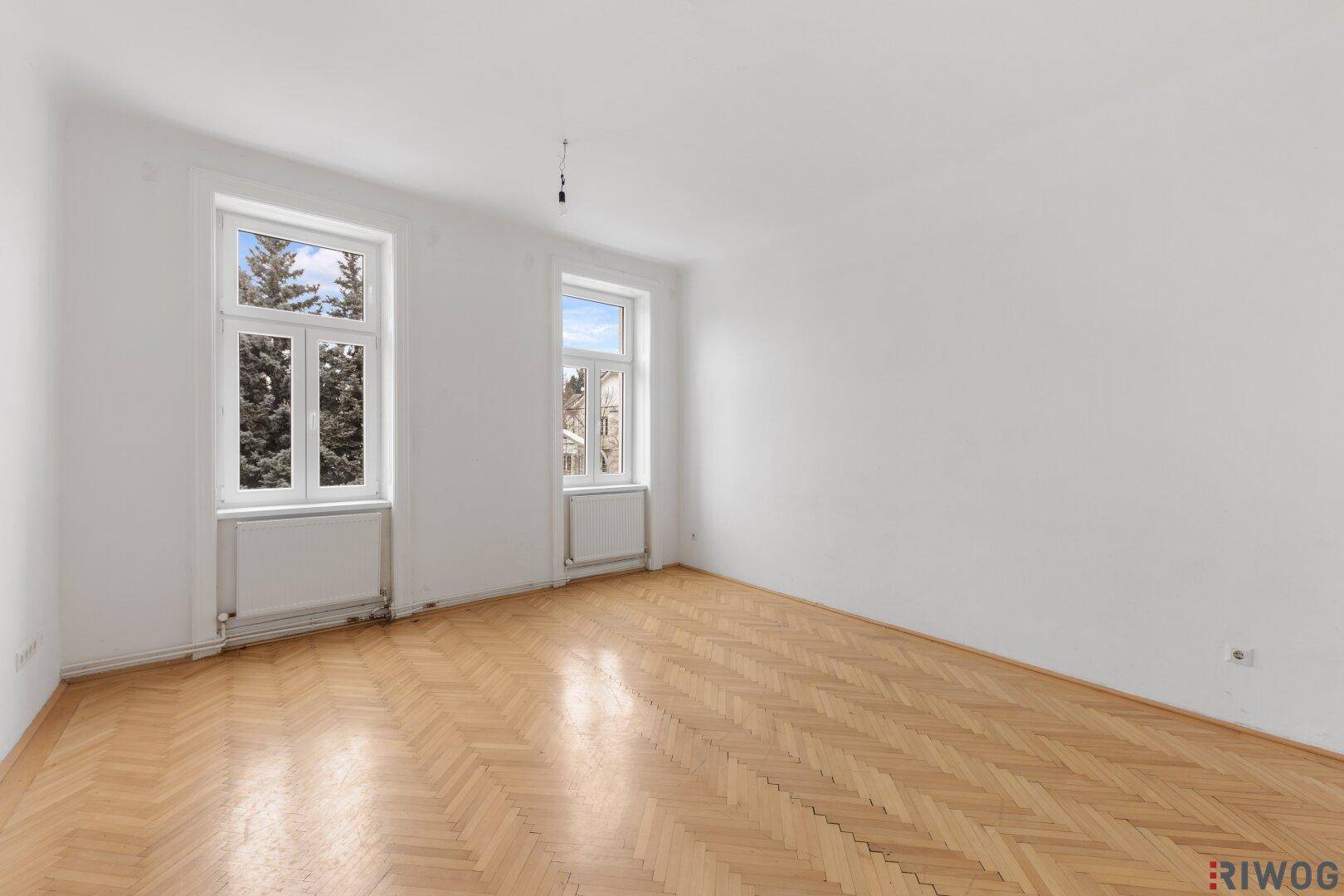 Helles Zimmer mit klassischem Fischgrätparkett und Blick auf Bäume.