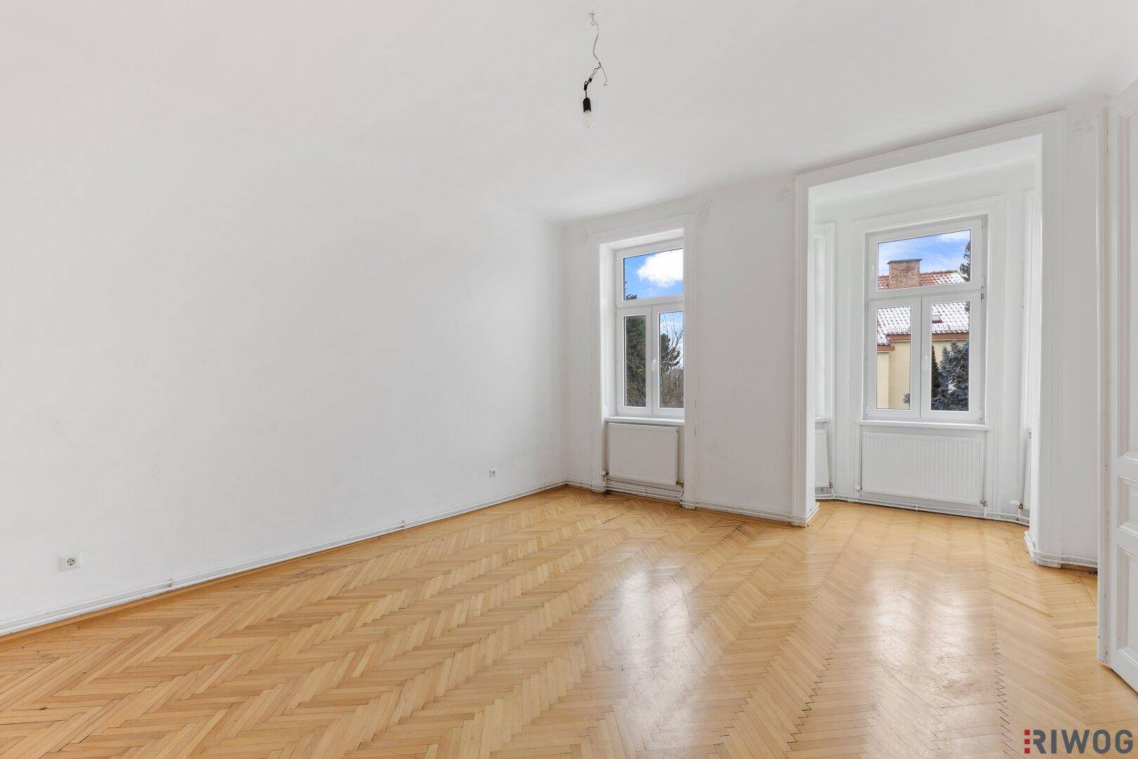 Geräumiges Zimmer mit Fischgrätparkett, hohen Fenstern und viel natürlichem Licht.