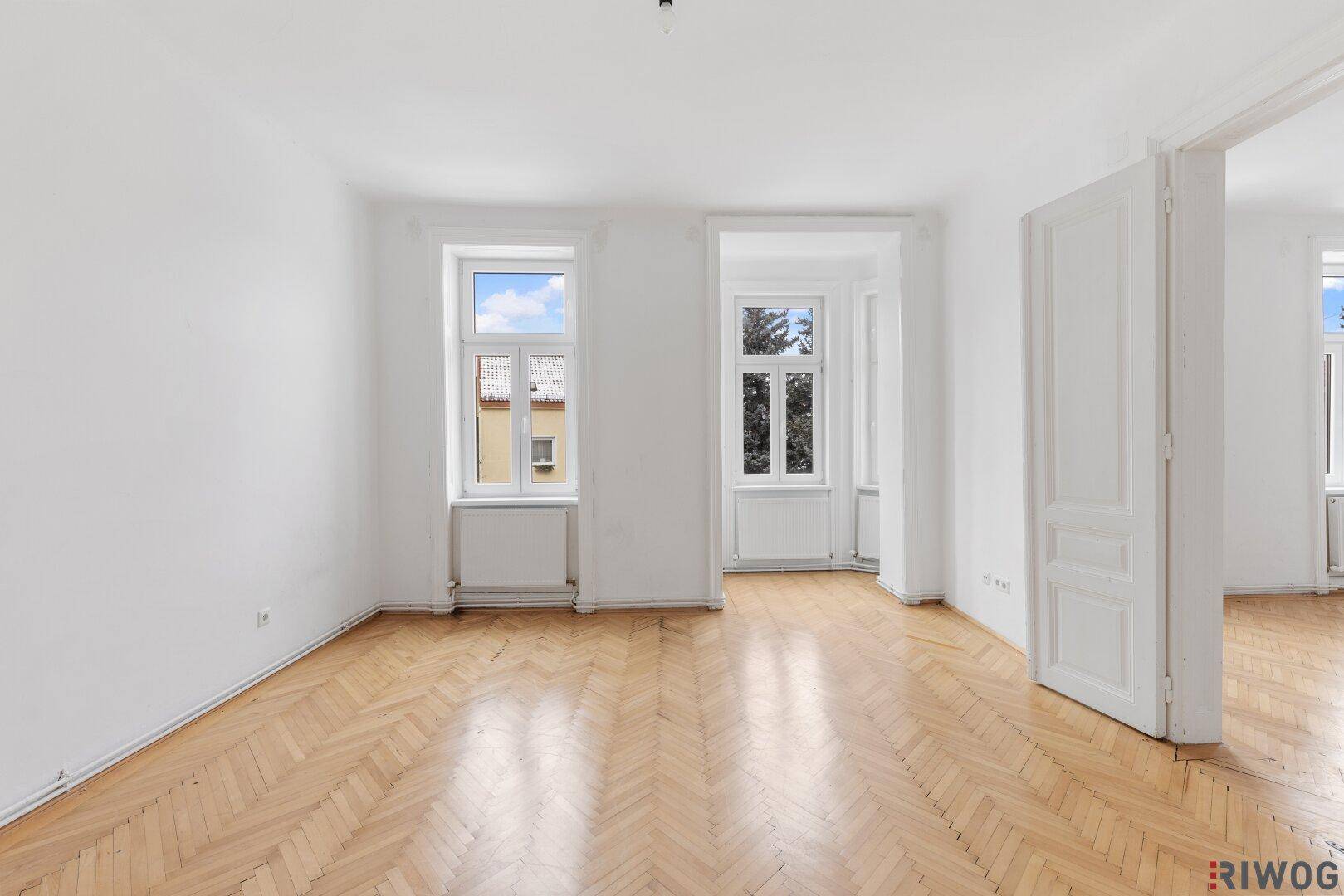 Geräumiges, helles Zimmer mit klassischem Fischgrätparkett und Blick nach draußen.