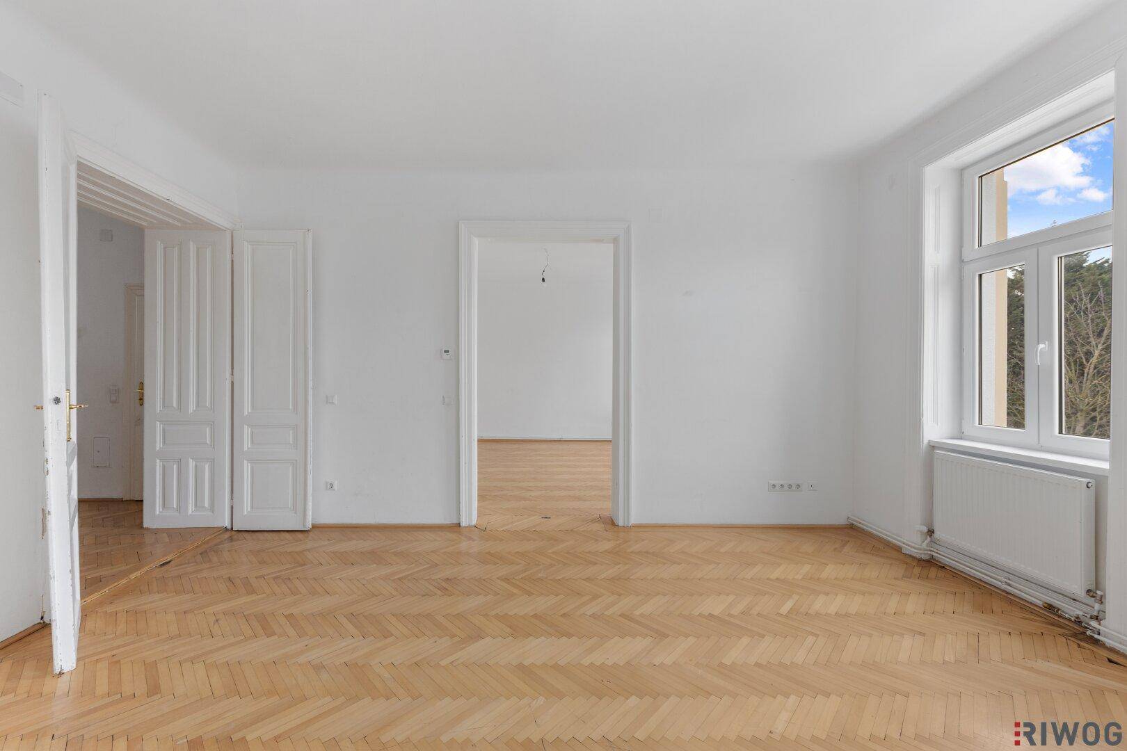 Helles Zimmer mit Parkettboden und Zugang zu angrenzenden Räumen.