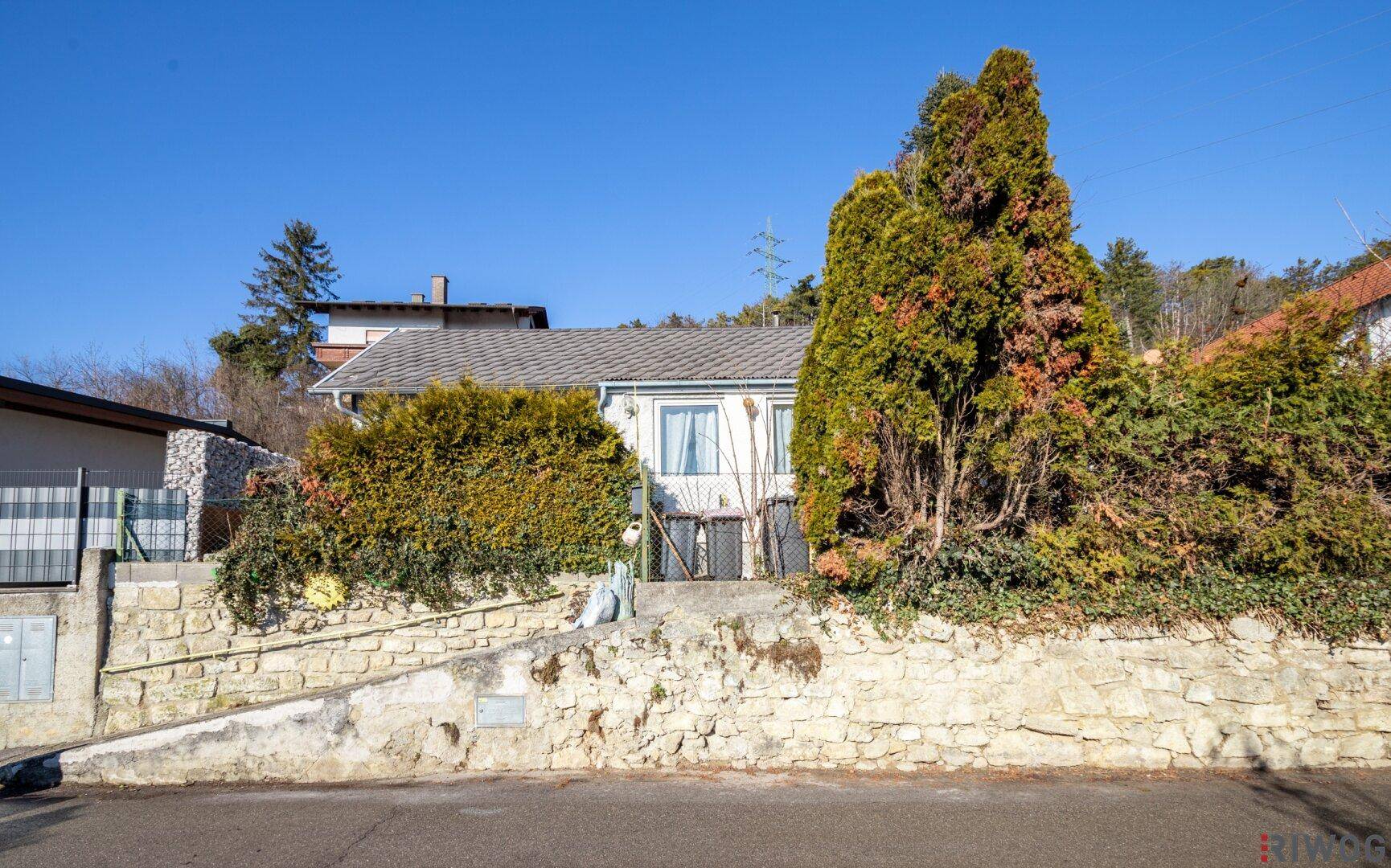 Ansicht des Hauses von der Straße mit einer Steinmauer und gepflegten Hecken.