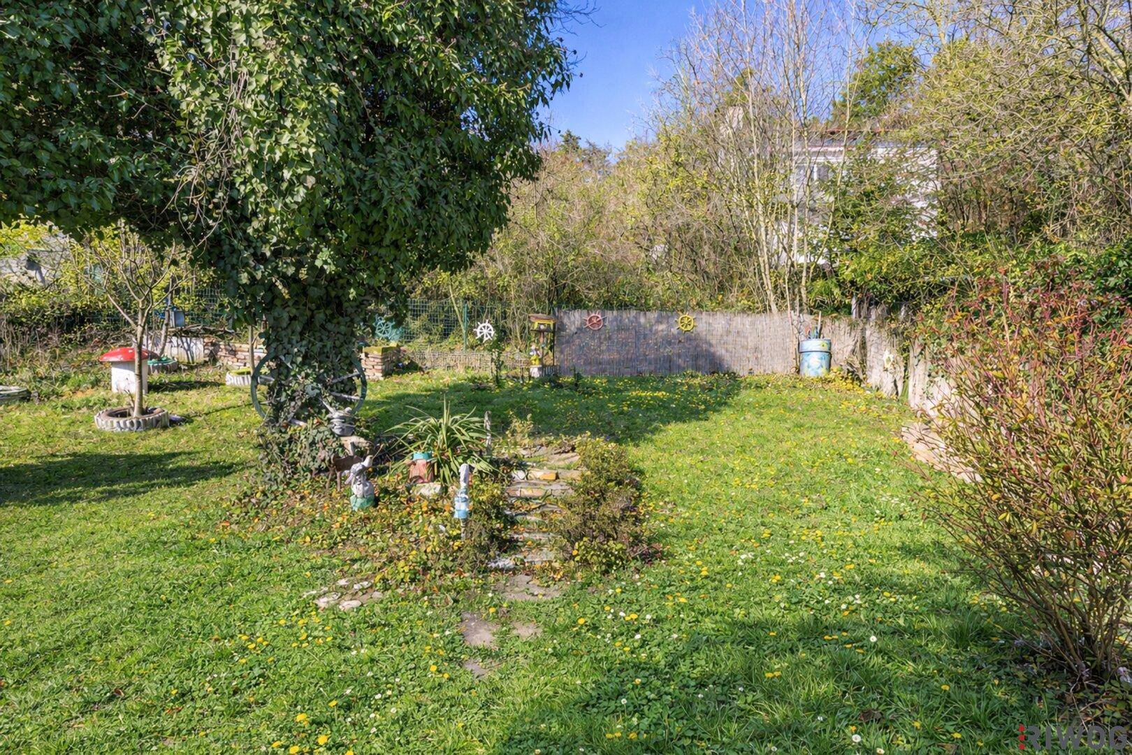 Gepflegter Gartenbereich mit Rasenfläche, kleinen Beeten und einer Steinmauer im Hintergrund.
