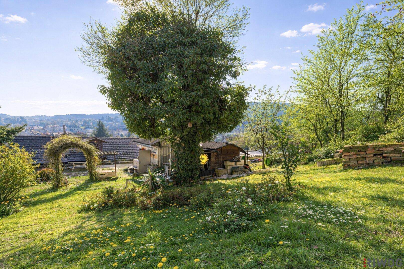 Weitläufiger Garten mit altem Baumbestand und Blick auf die umliegende Landschaft und Häuser.
