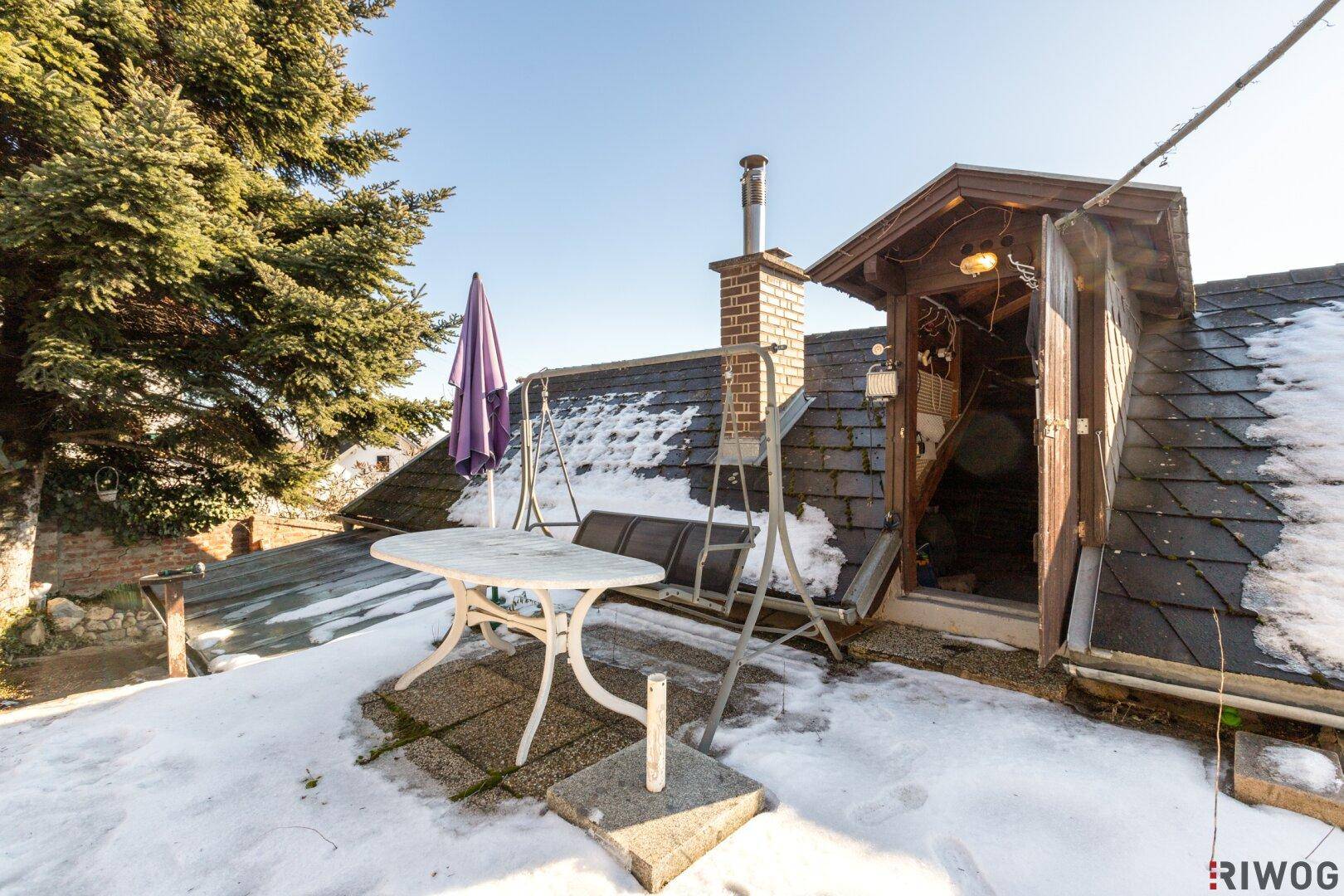 Kleine Dachterrasse mit Tisch und Sonnenschirm, teilweise mit Schnee bedeckt, neben dem Dachausgang.