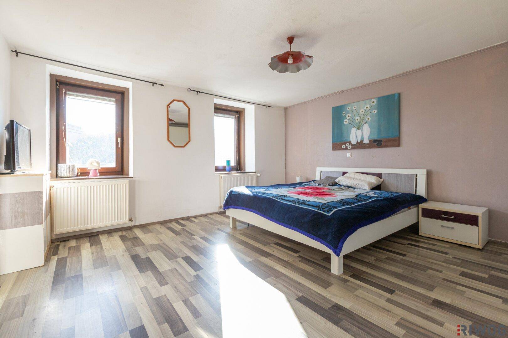 Geräumiges Schlafzimmer mit Laminatboden, zwei Fenstern und einem Doppelbett.