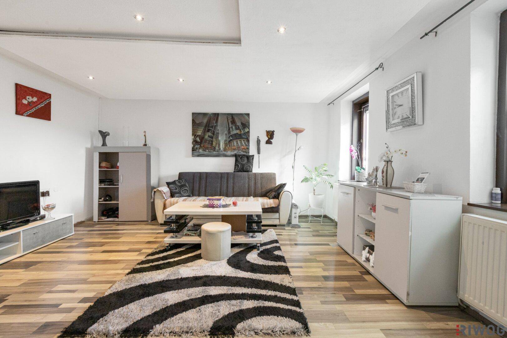 Modern eingerichtetes Wohnzimmer mit Laminatboden, Sofa und Deckenstrahlern.