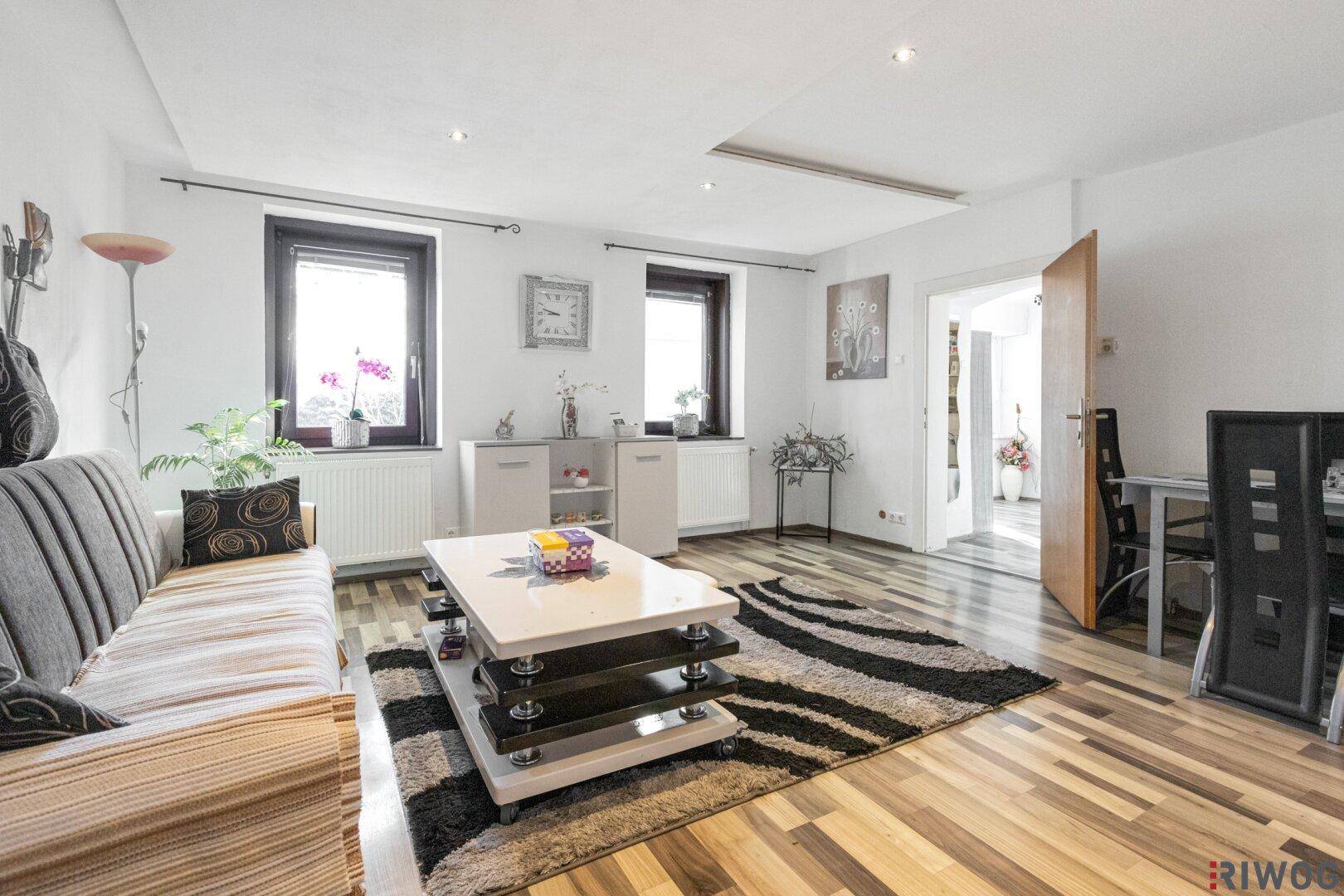 Gemütliches Wohnzimmer mit Laminatboden, Couch und Blick auf den Essbereich.