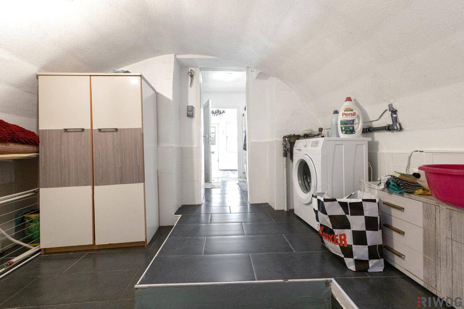 Waschküche im Kellerbereich mit Waschmaschine, Stauraum und Fliesenboden.