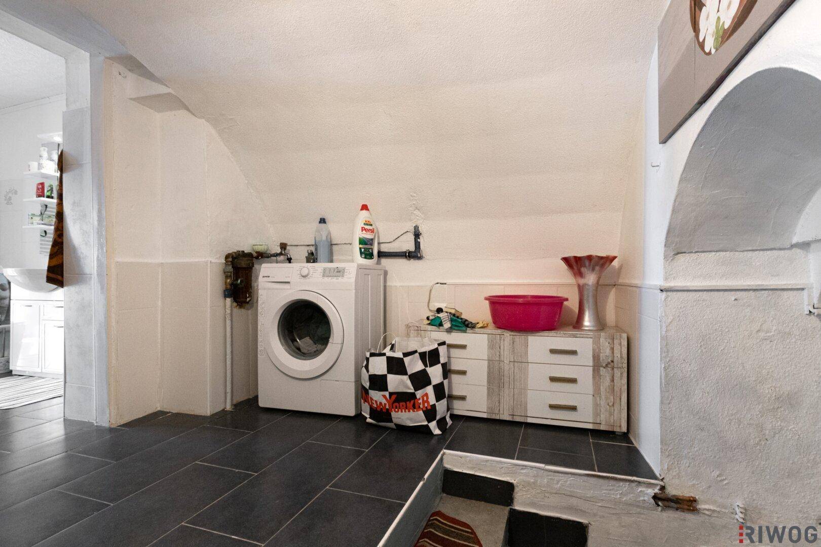 Kellerraum mit Waschmaschine, Stauraum und gewölbter Decke, ideal für Haushaltsarbeiten.