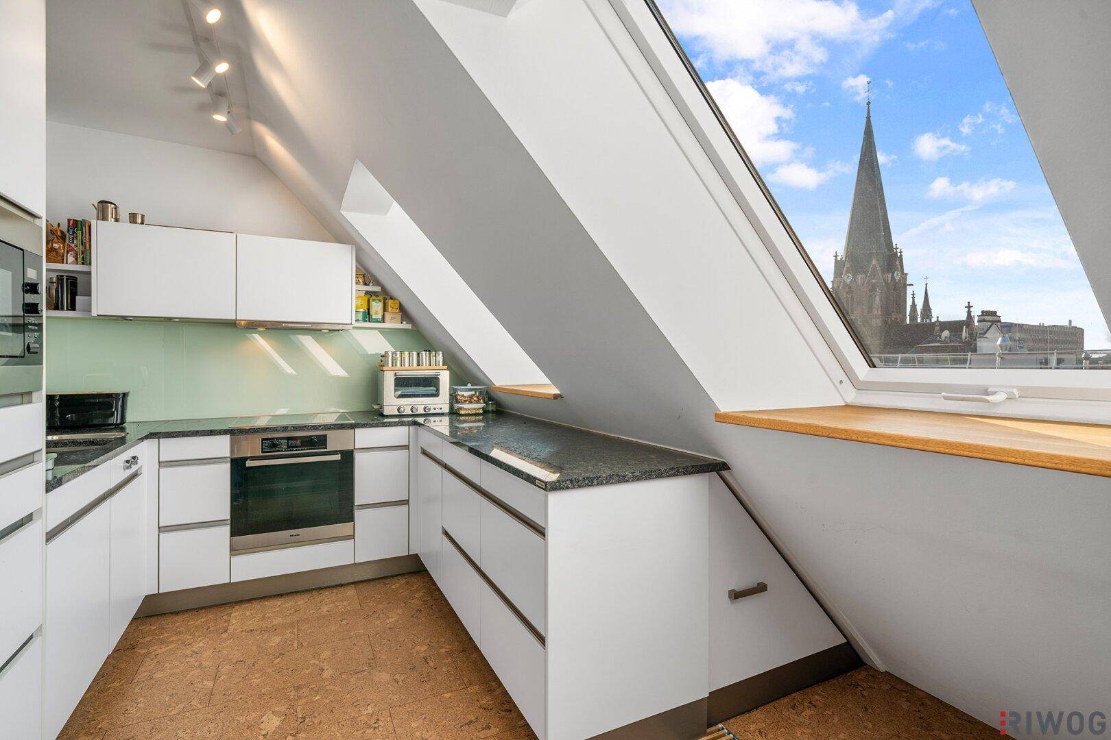 Moderne Küche im Dachgeschoss mit weißen Schränken, Granitarbeitsplatte und Blick auf die Stadt.