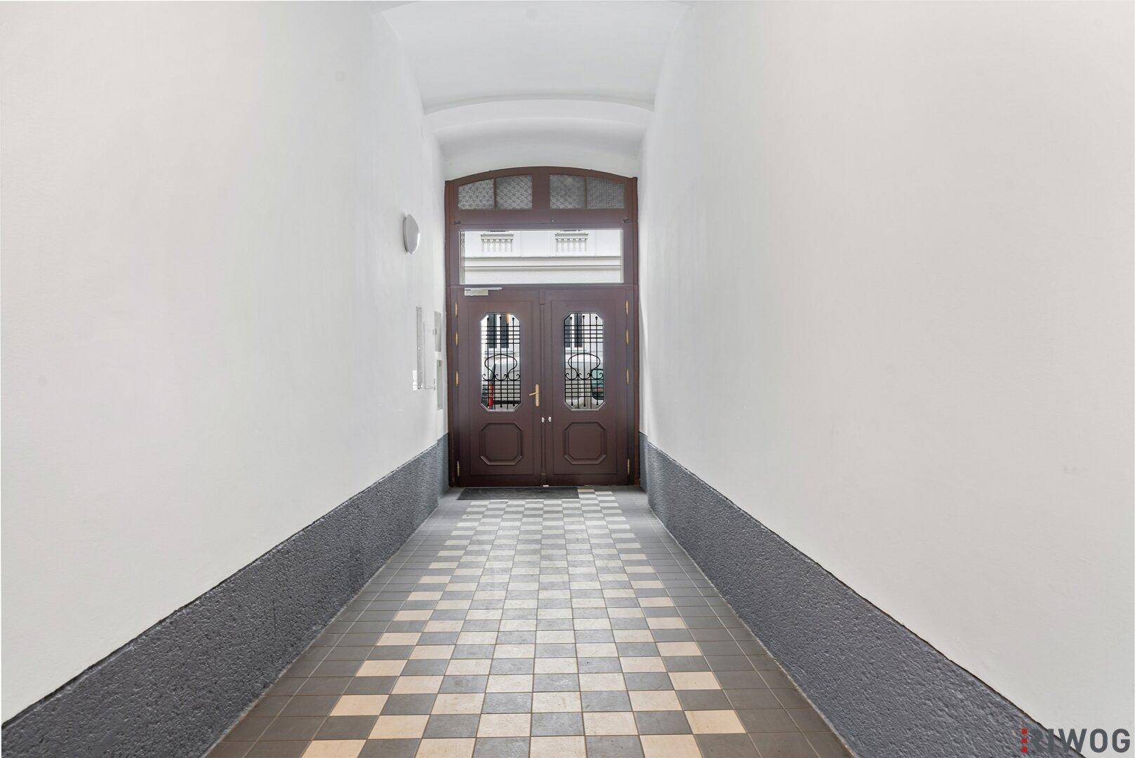 Eingangsbereich mit traditionellem Fliesenboden und Holztüren, der in das Gebäude führt.