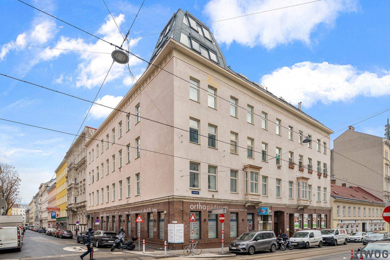 Historisches Eckgebäude mit moderner Dachaufstockung in einer belebten Stadtstraße.