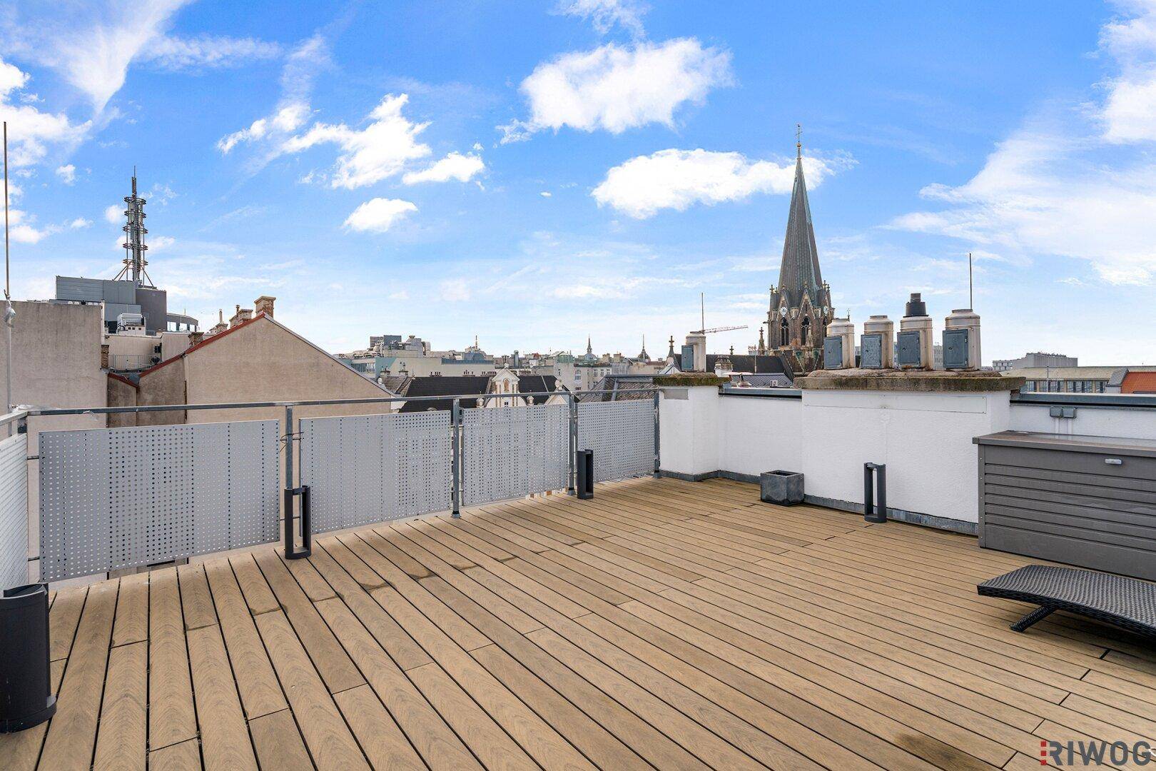 Geräumige Dachterrasse mit Holzboden und weitem Blick über die Dächer der Stadt.