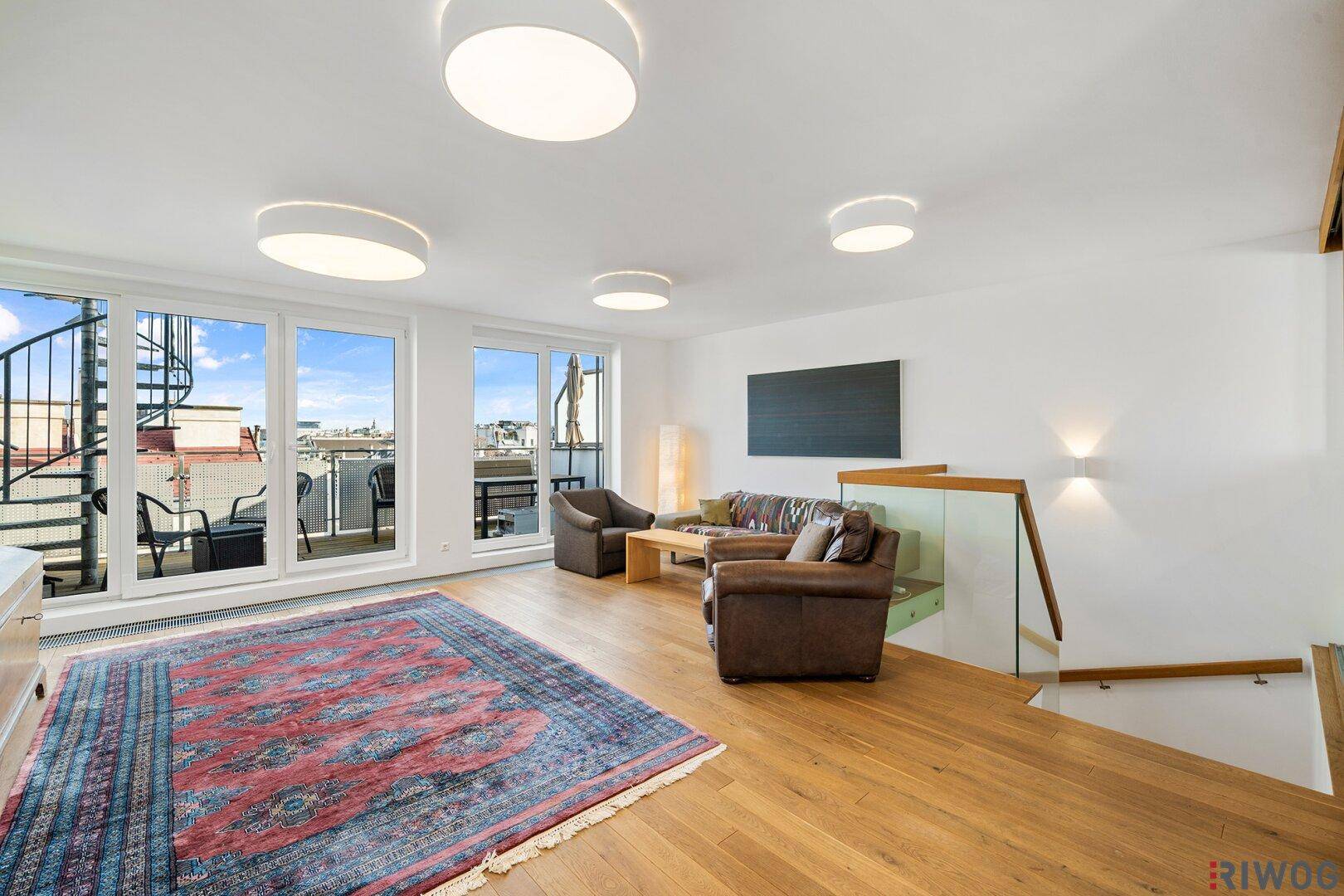 Geräumiges Wohnzimmer mit Holzboden, großen Fenstern und Zugang zu einer Außenterrasse.