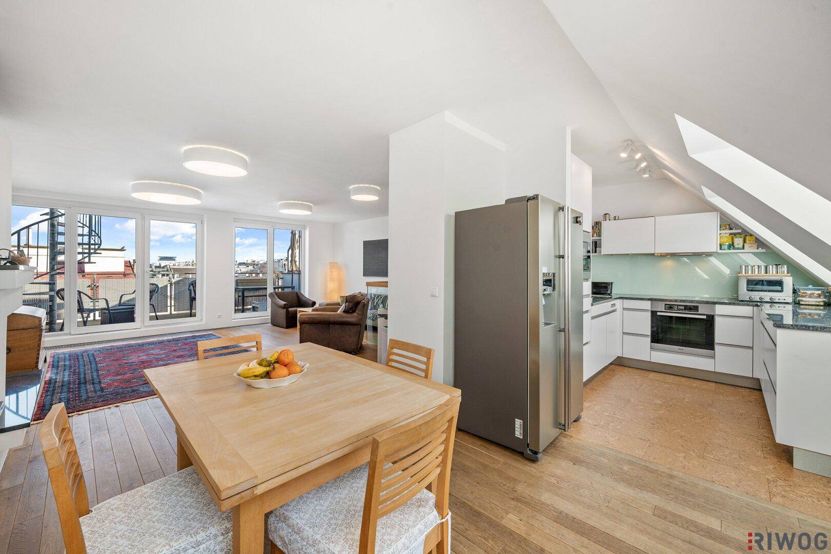 Offener Wohn-Essbereich mit moderner Küche, Holzboden und Zugang zu einer Terrasse mit Stadtblick.