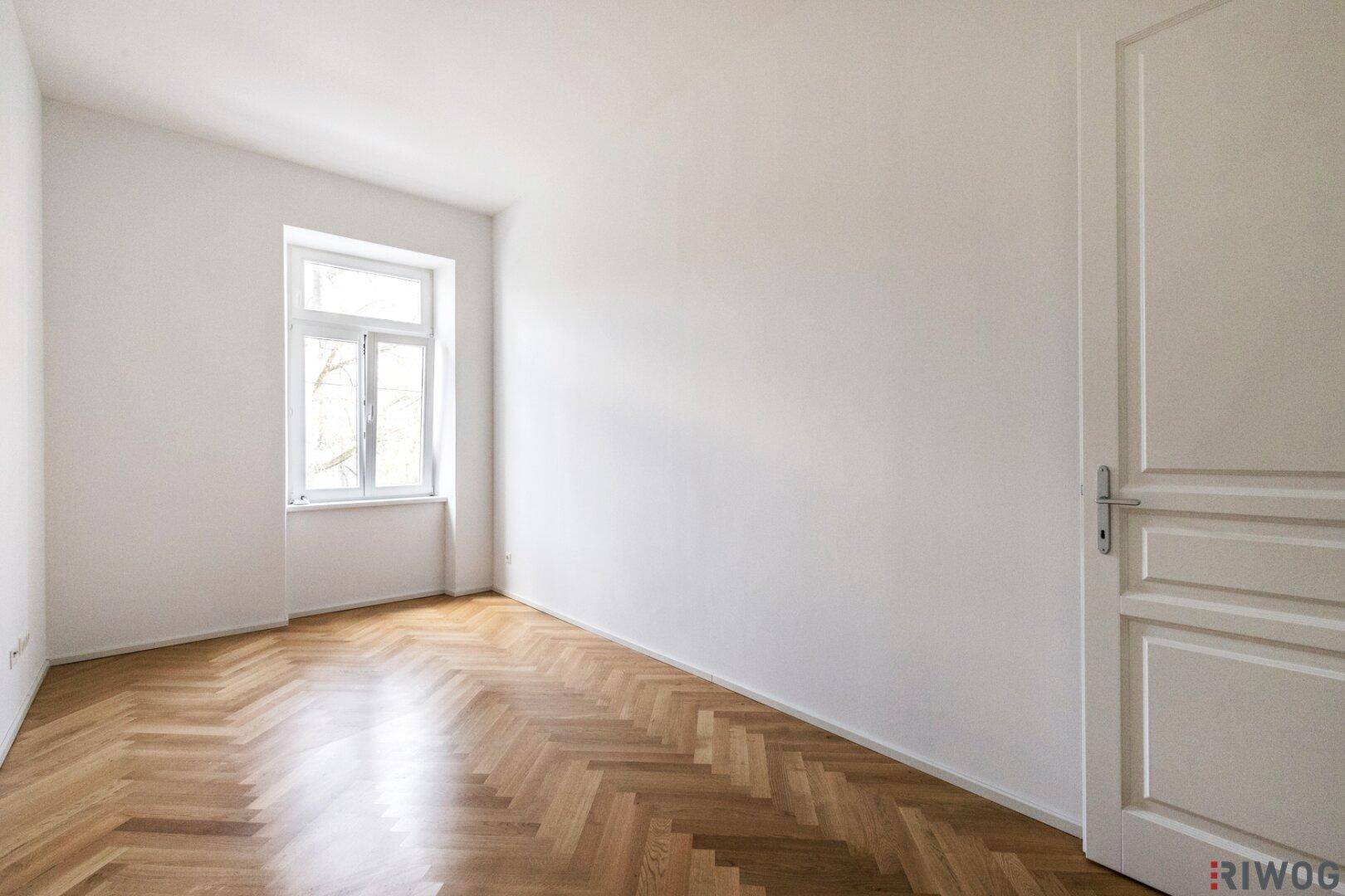Helles Zimmer mit klassischem Fischgrätparkett und großem Fenster für viel Tageslicht.