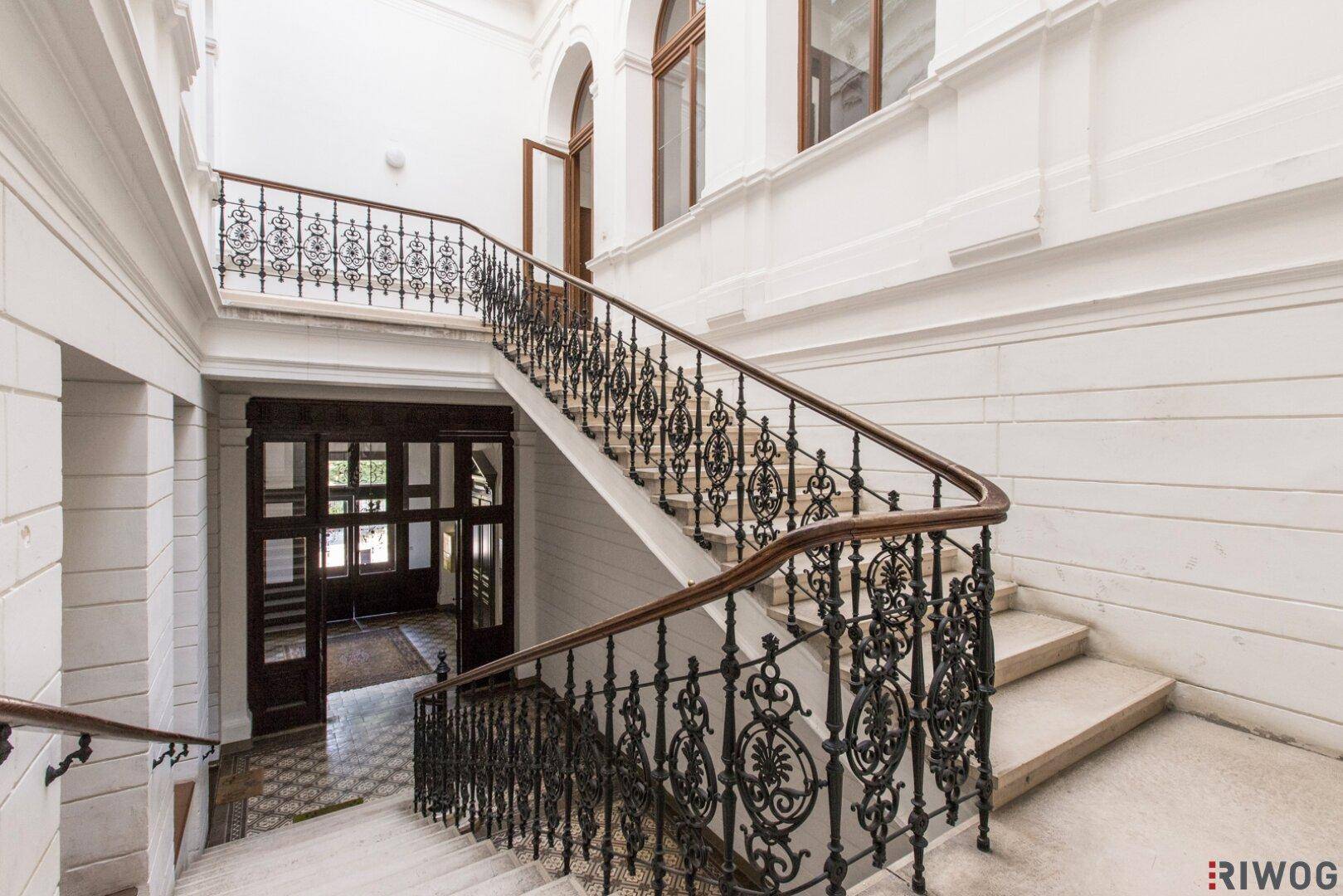 Elegantes Treppenhaus mit Marmorstufen, schmiedeeisernem Geländer und hohen Decken.