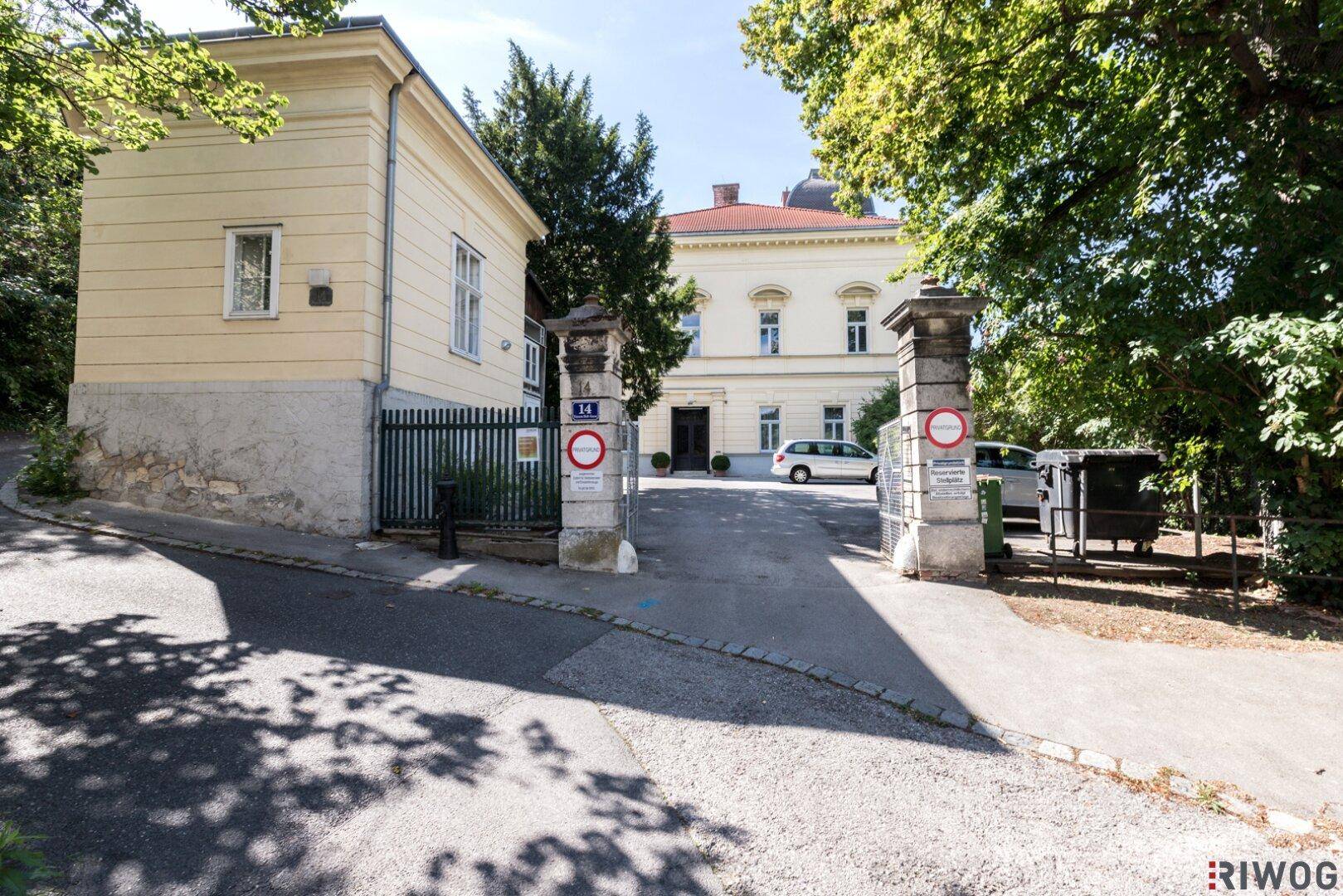 Einfahrt zur historischen Villa mit Nebengebäude und altem Baumbestand in sonniger Lage.