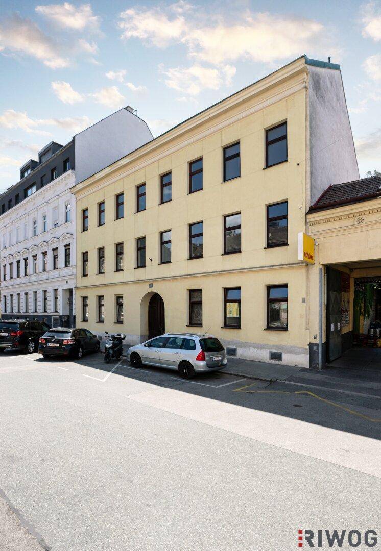 Gelbes Mehrfamilienhaus mit klassischer Architektur und geparkten Autos an einer Straße.