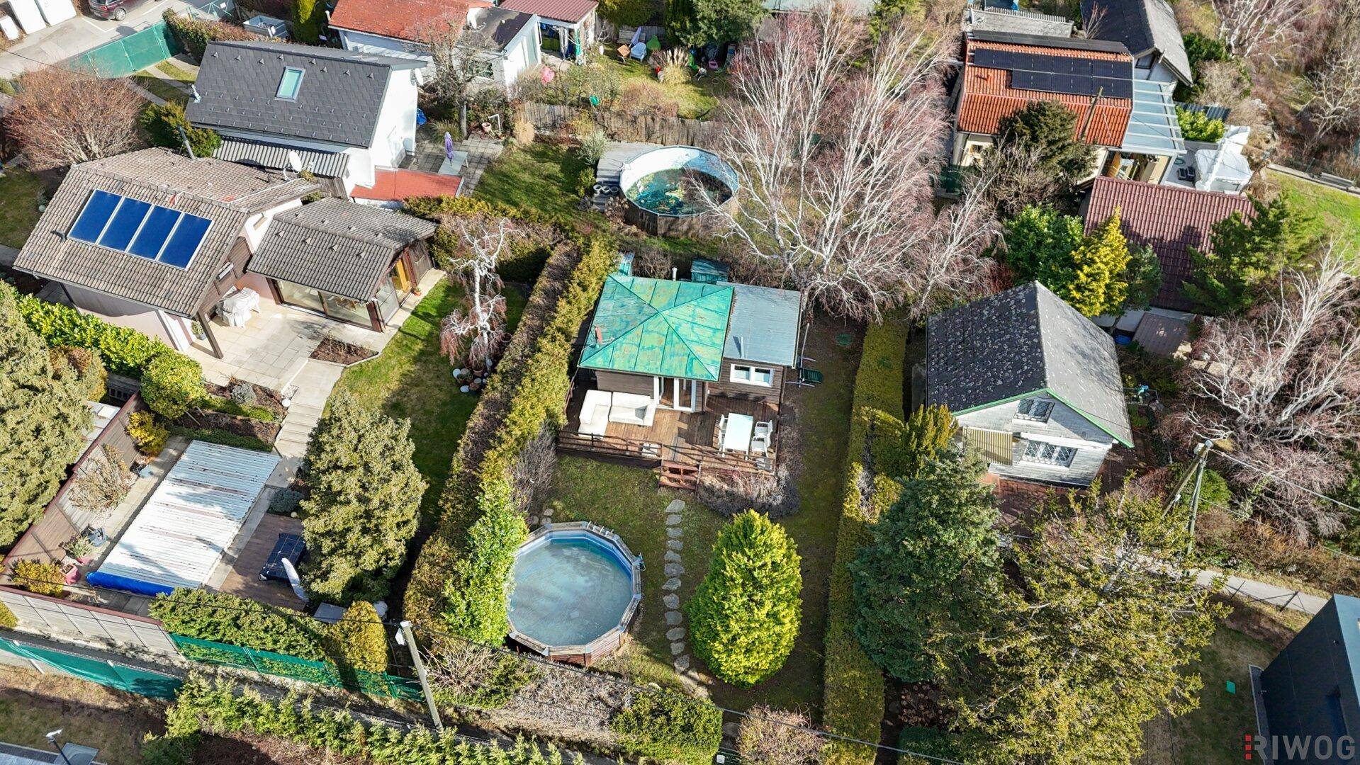 Luftaufnahme eines Wohnhauses mit Garten, Holzterrasse und Swimmingpool, umgeben von weiteren Wohnhäusern.