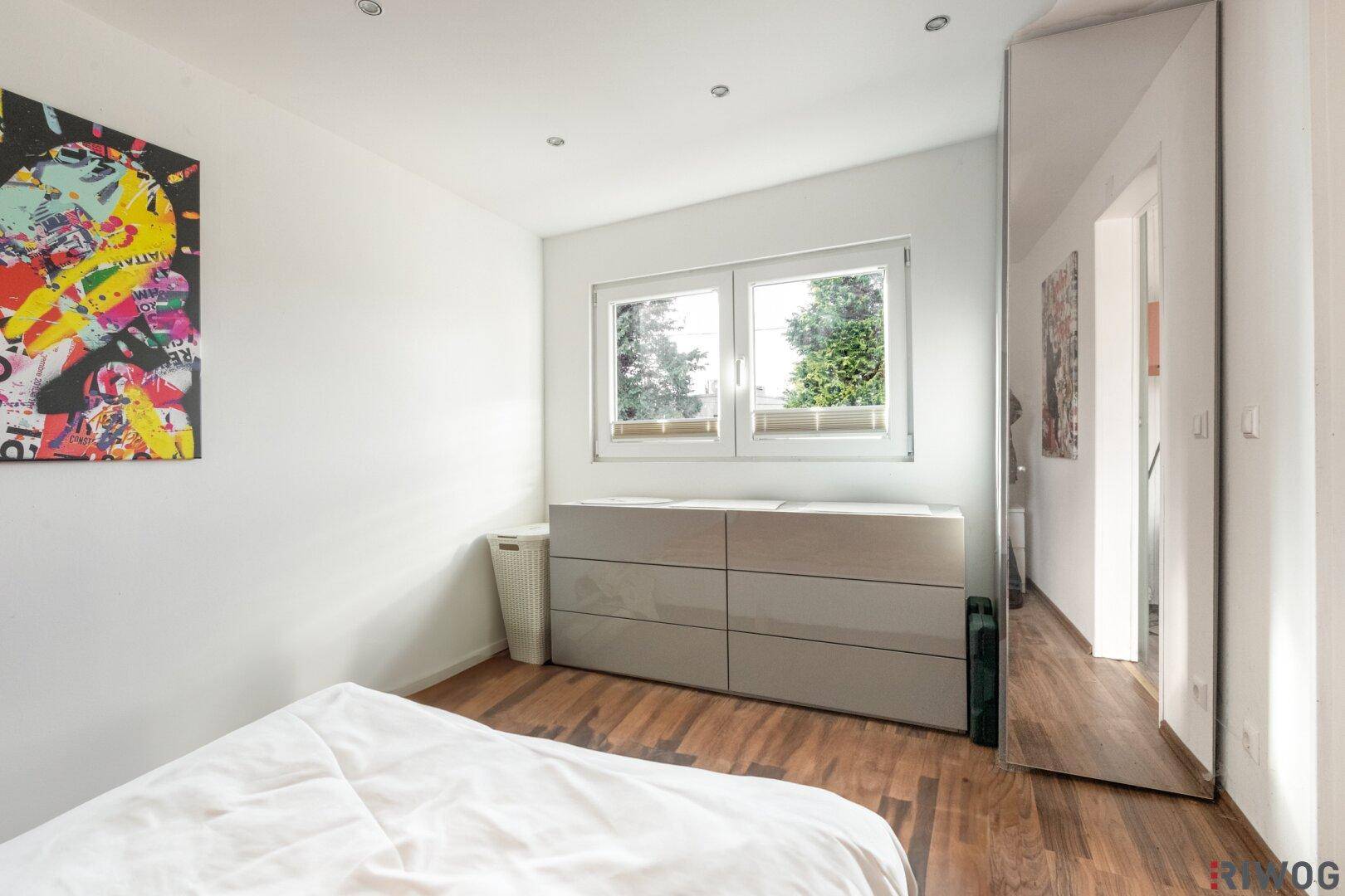 Schlafzimmer mit Fenster, das viel Tageslicht hereinlässt, und einem modernen Sideboard.