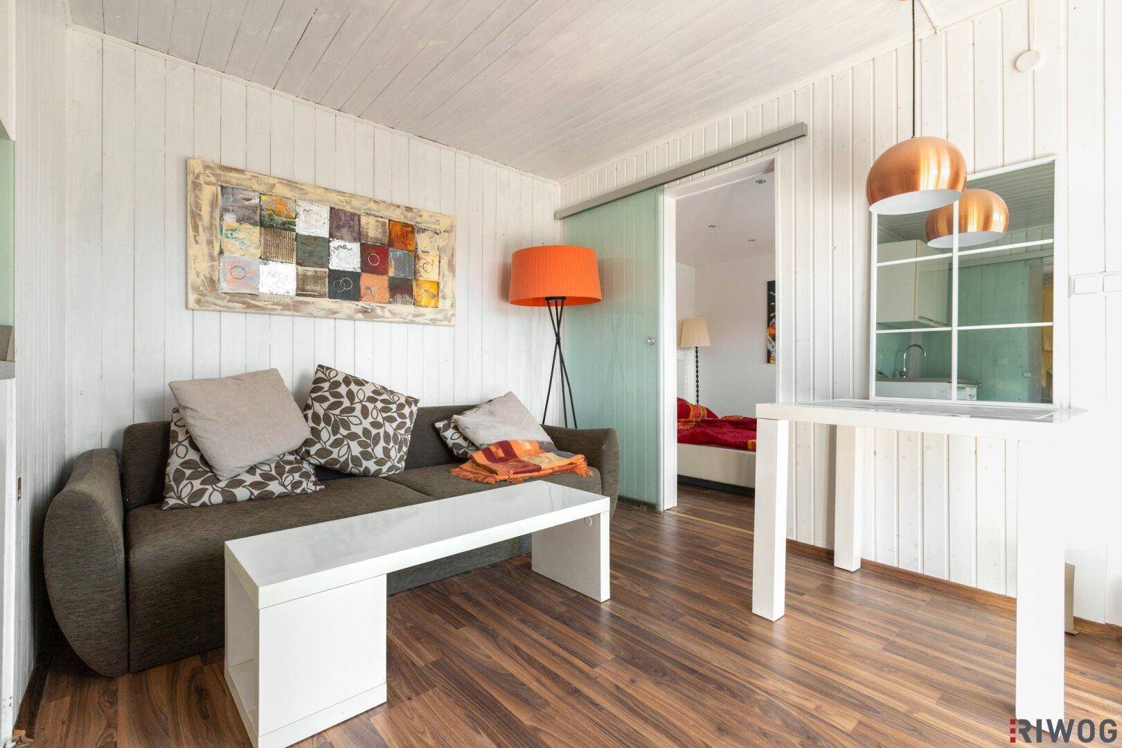 Heller Wohnbereich mit Sofa, Esstisch und Blick durch die Schiebetür in ein Schlafzimmer.