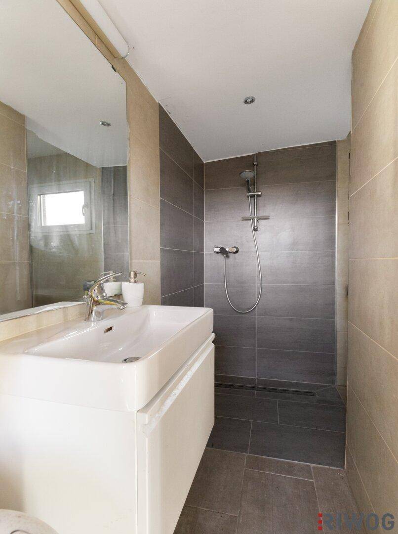 Modernes Badezimmer mit Waschtisch, großem Spiegel und ebenerdiger Dusche.