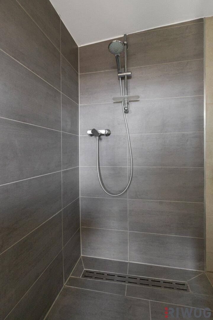 Ebenerdige Dusche mit modernen grauen Fliesen und Duscharmatur.