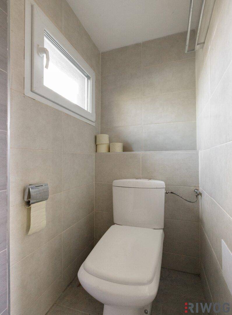 Separates WC mit Toilette, Fenster und hellen Fliesen an den Wänden.