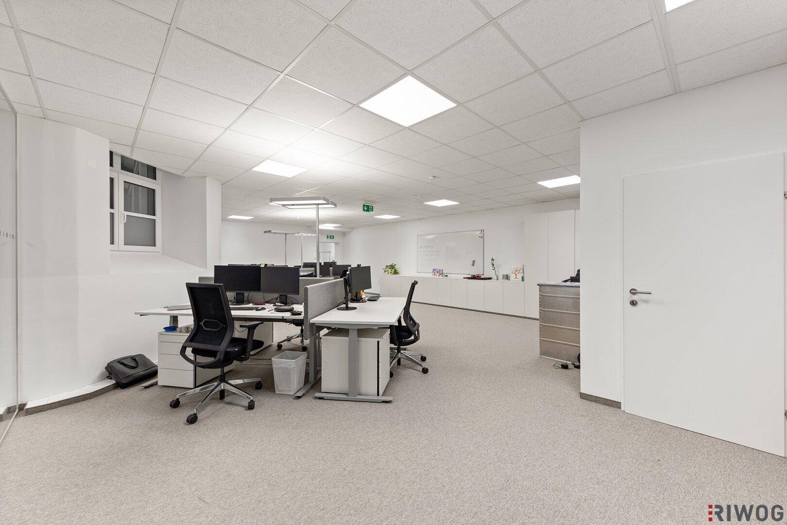 Helles Großraumbüro mit modernen Arbeitsplätzen, Teppichboden und abgehängter Decke.